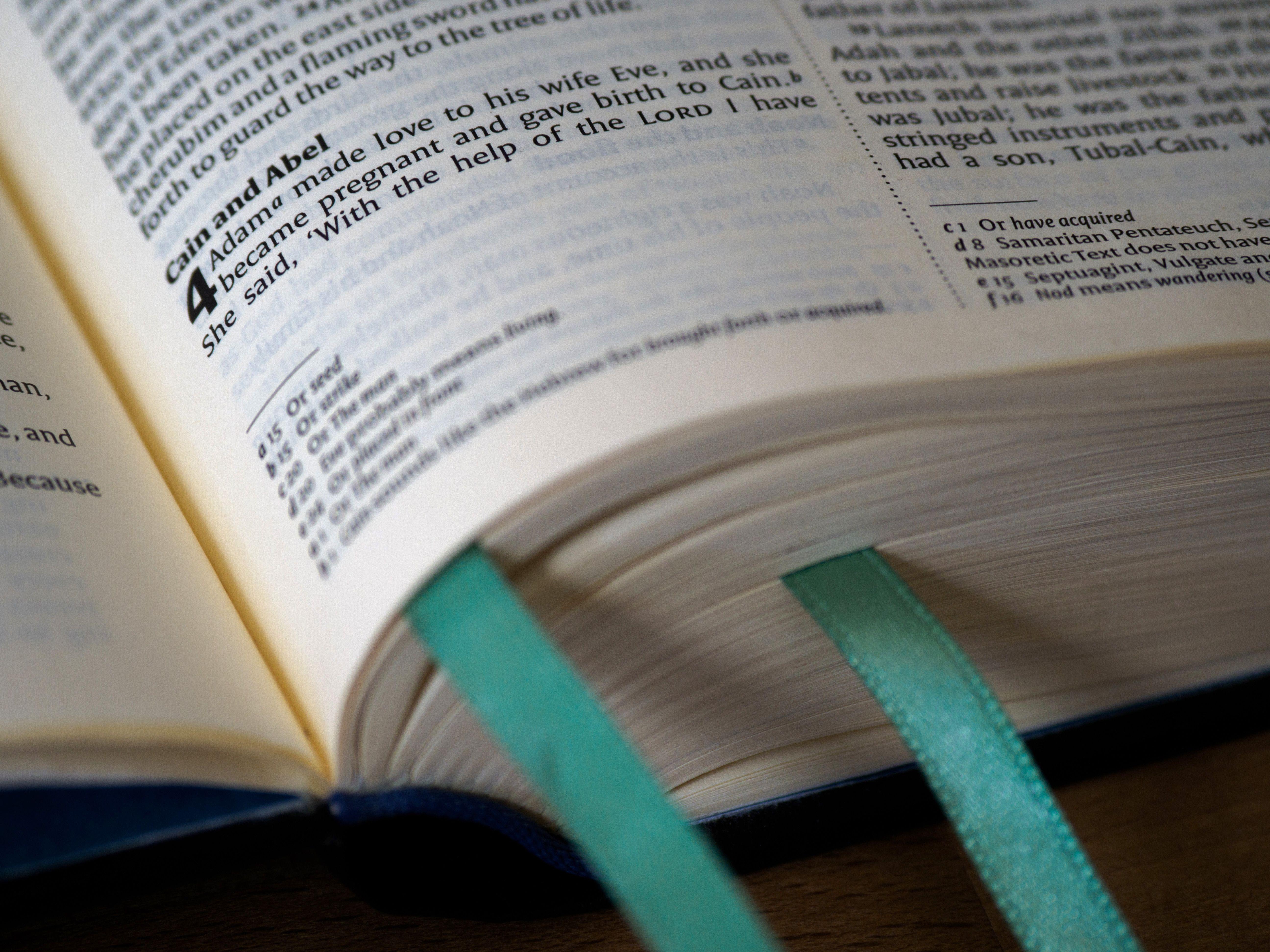 Open Bible showing Genesis, Cain and Abel story, with teal bookmarks.