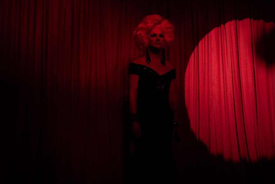 A captivating drag queen in a glamorous black dress on stage with red lighting, capturing nightlife performance.