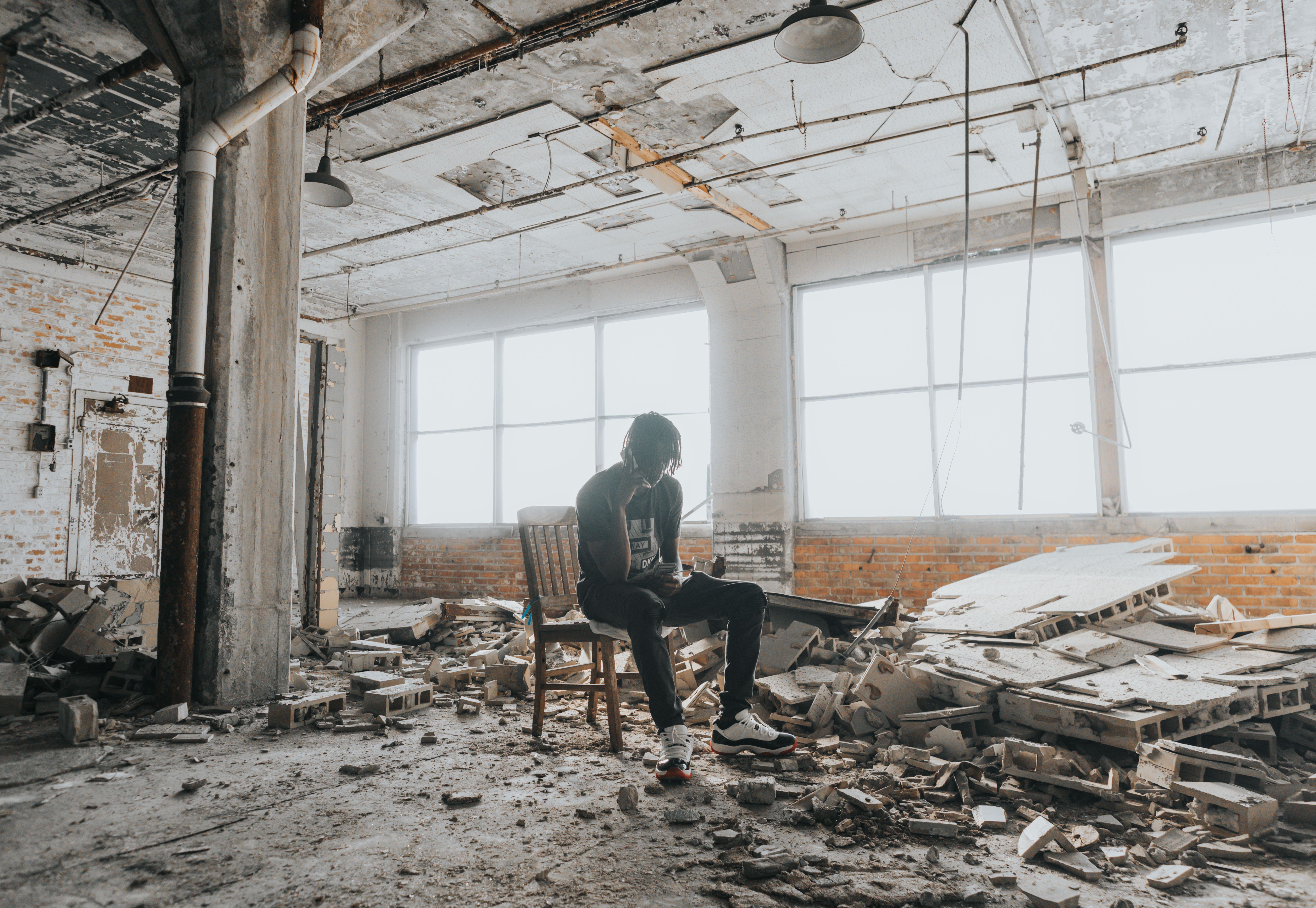 A person sits in a desolate, crumbling space filled with debris, conveying a powerful sense of abandonment.