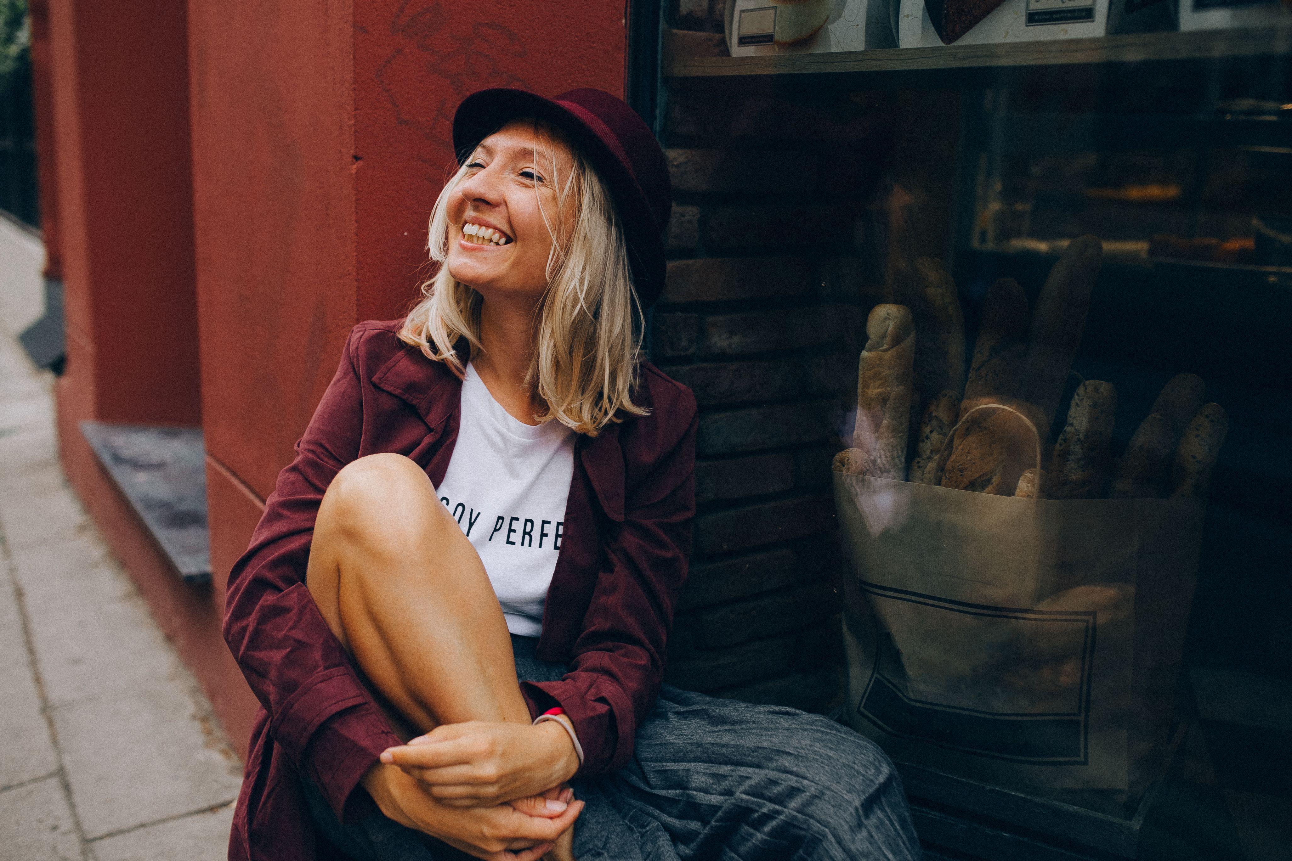 A happy woman sits by a bakery window, embracing a relaxed urban vibe.