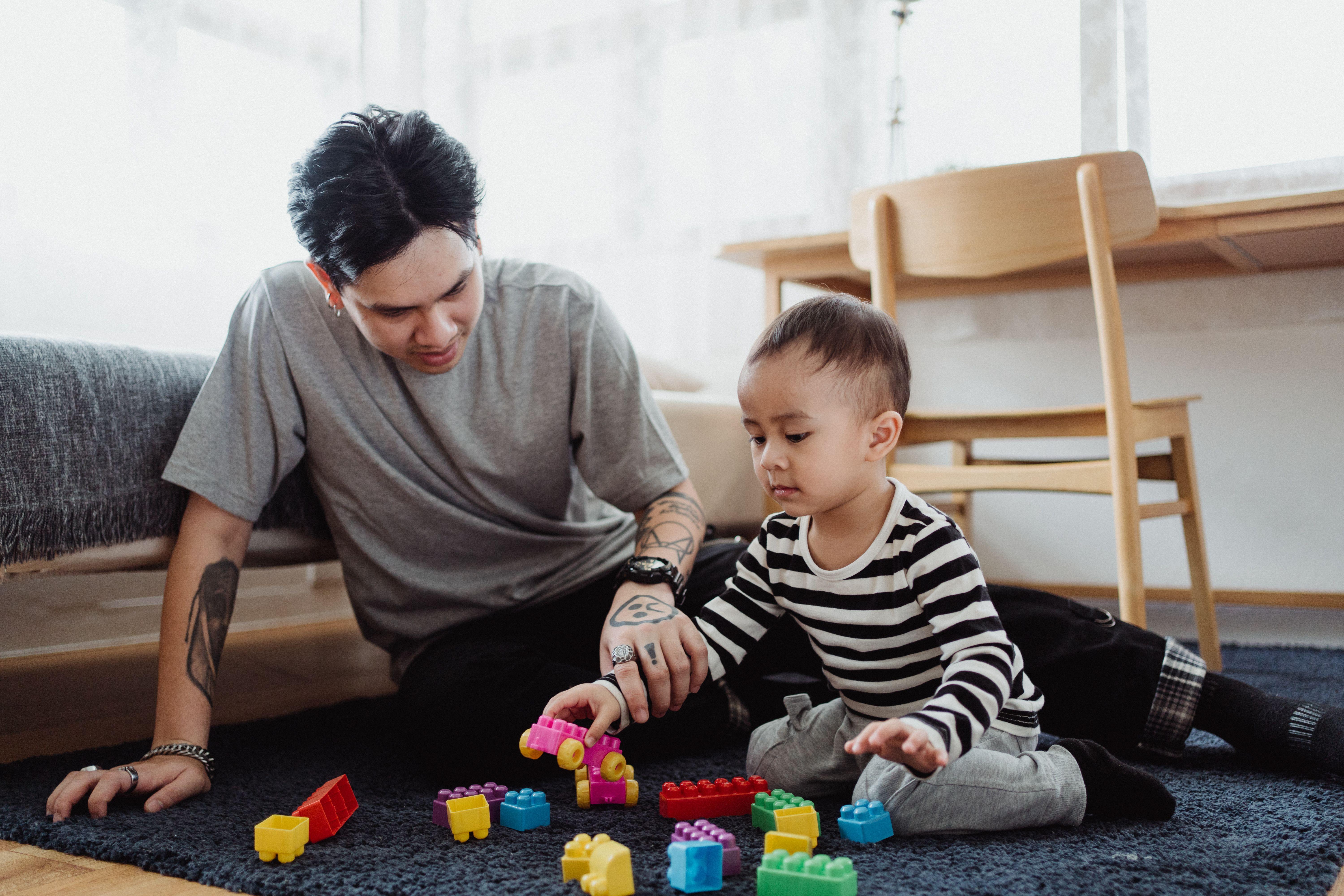 A father and son playing with colorful building blocks in a cozy indoor setting.