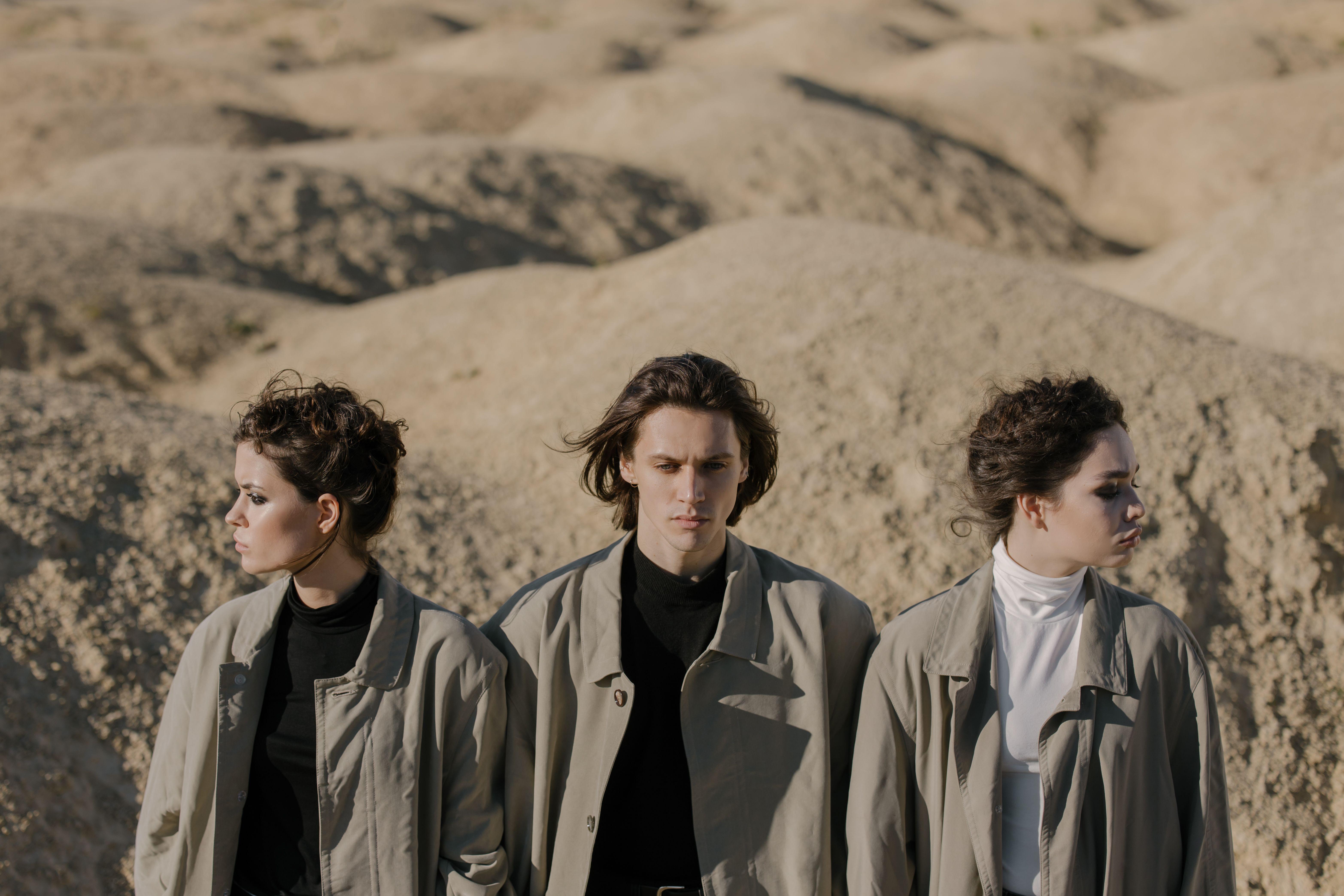Fashionable group wearing overcoats stands in a desert setting.