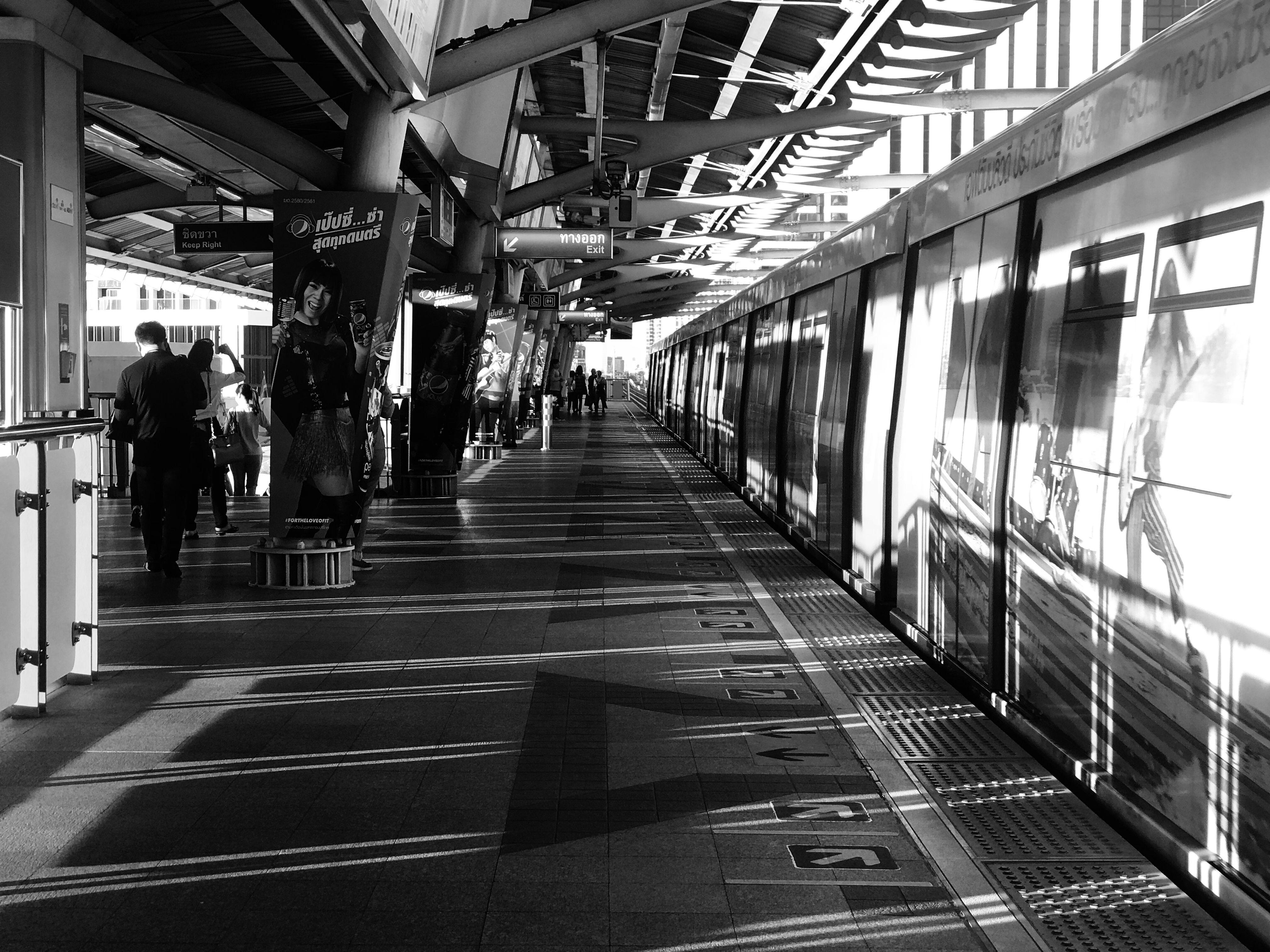 Black and white image capturing commuters at a railway platform in Khwaeng Samsen Nai, Bangkok, Thailand.