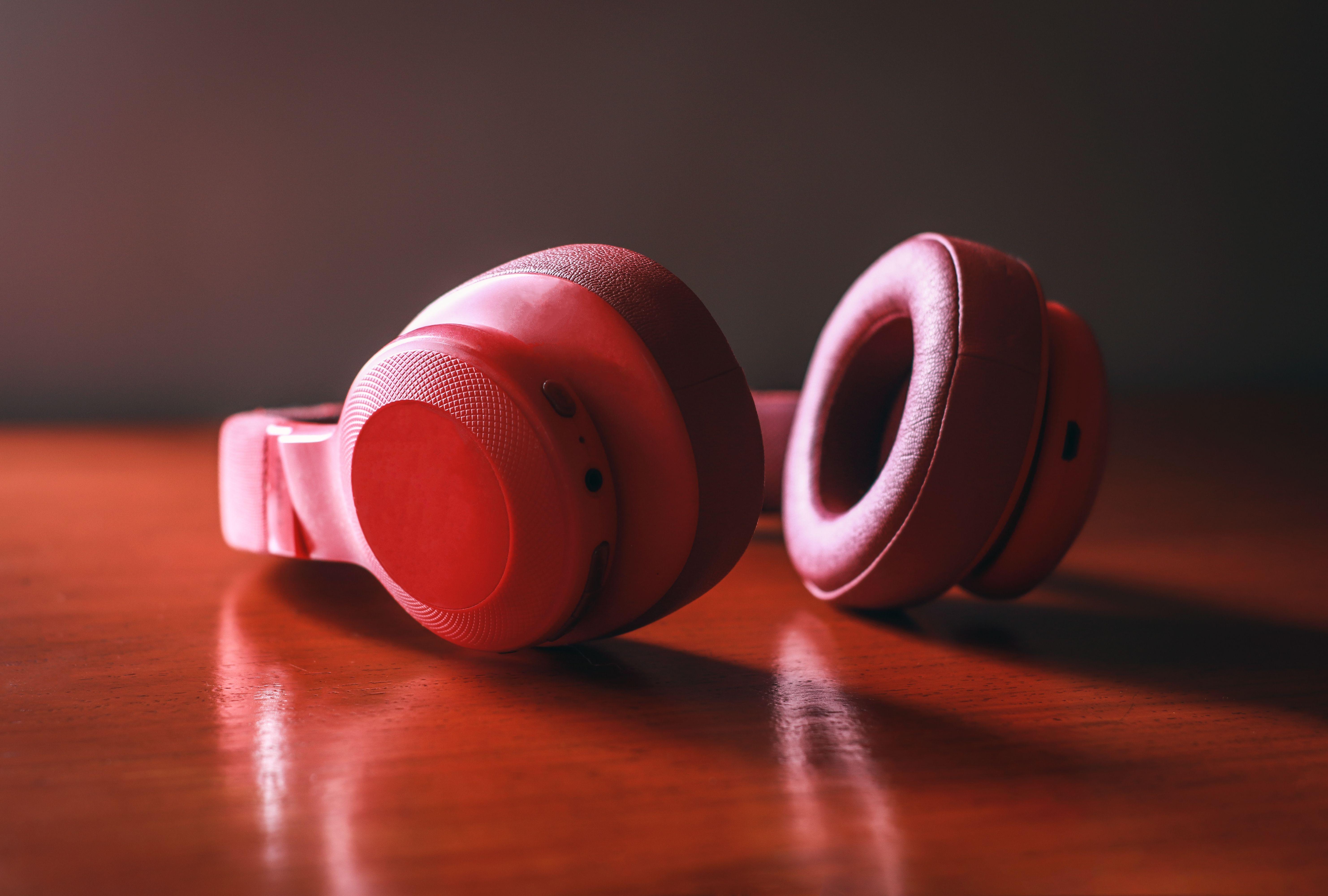 Close-up of red wireless headphones resting on a wooden surface, highlighting sleek design and vibrant color.