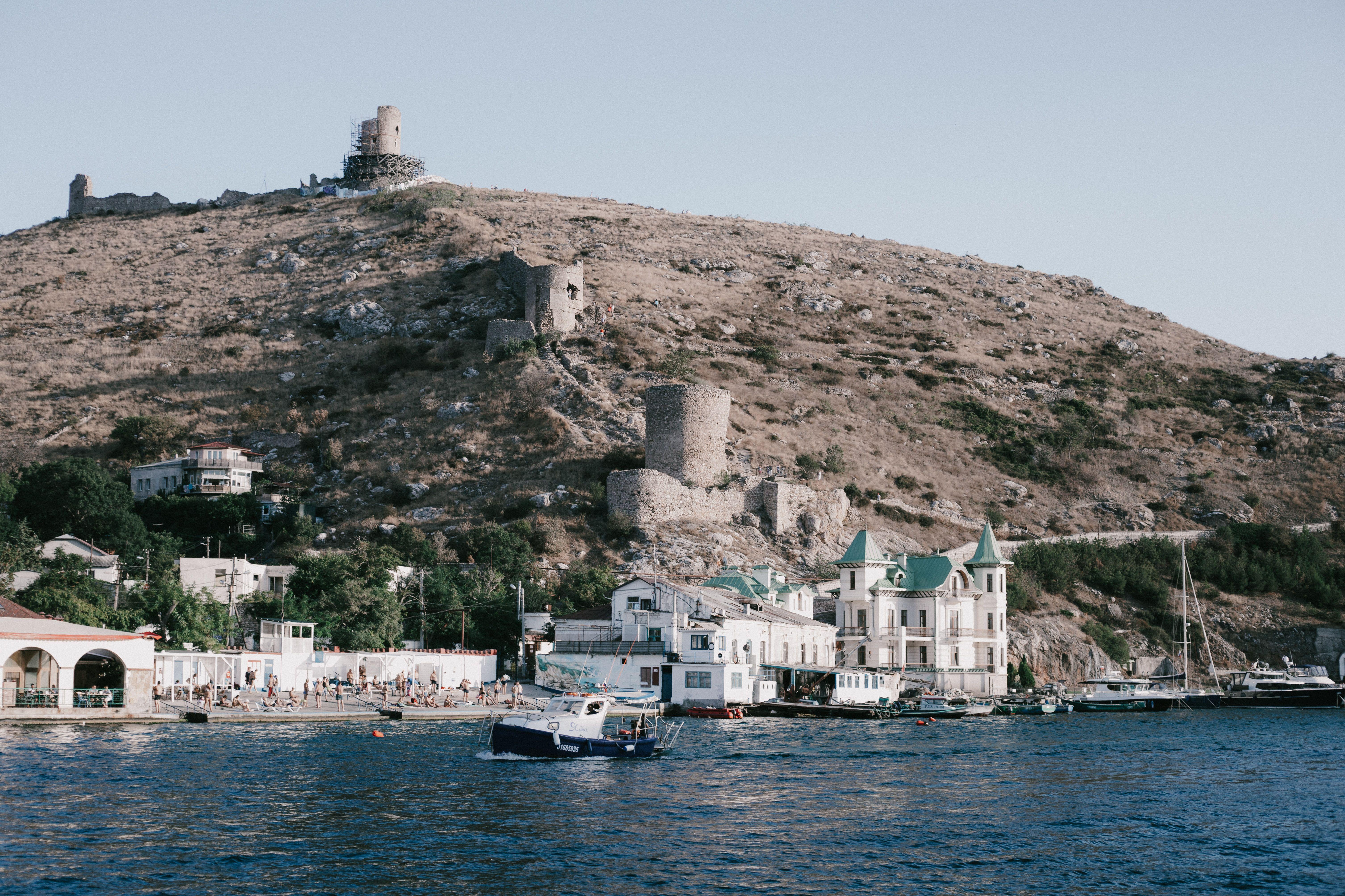 Scenic view of a historic coastal town with boats anchored at the harbor against hilly ruins.