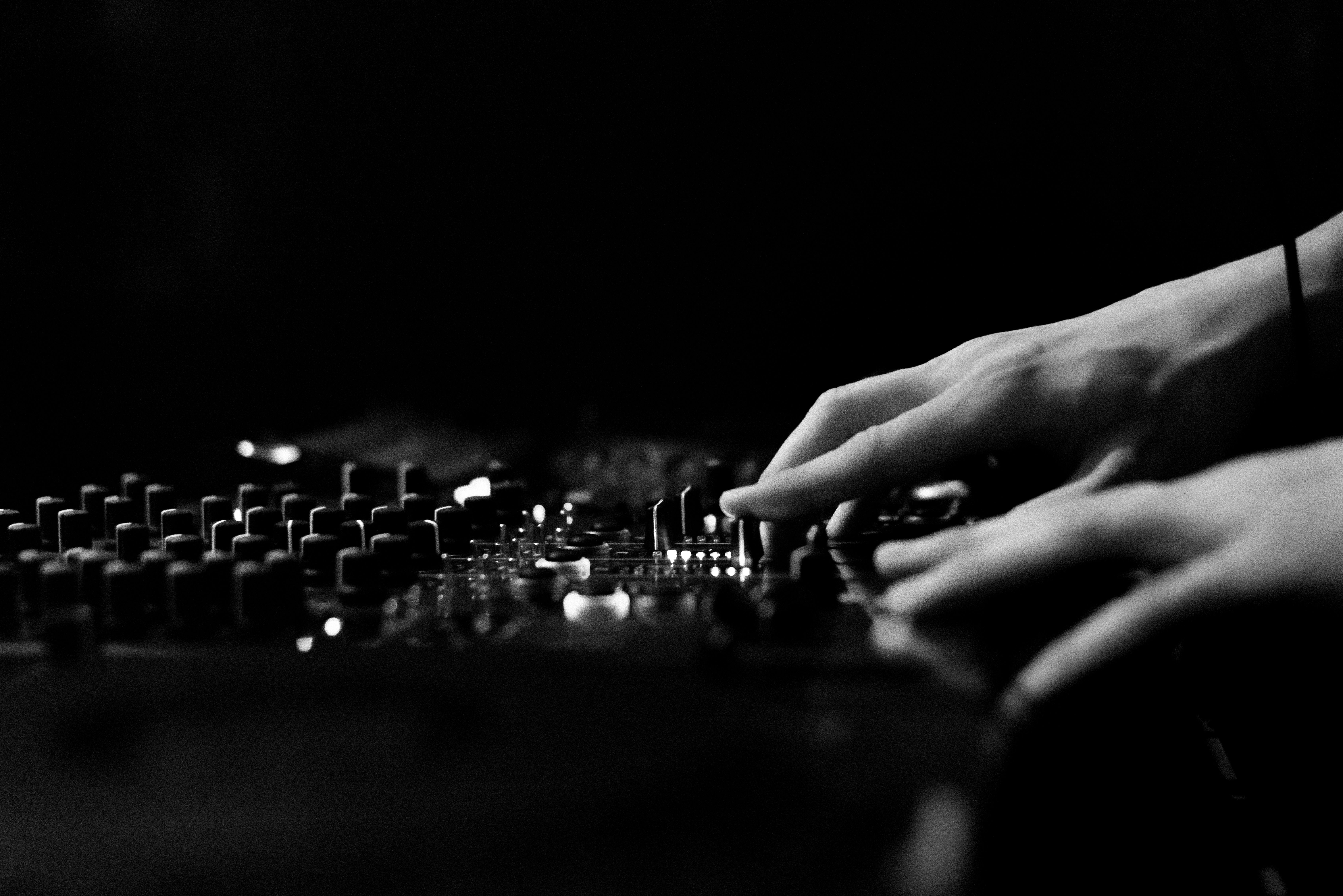 Artistic black and white image of hands adjusting a DJ console in a club.
