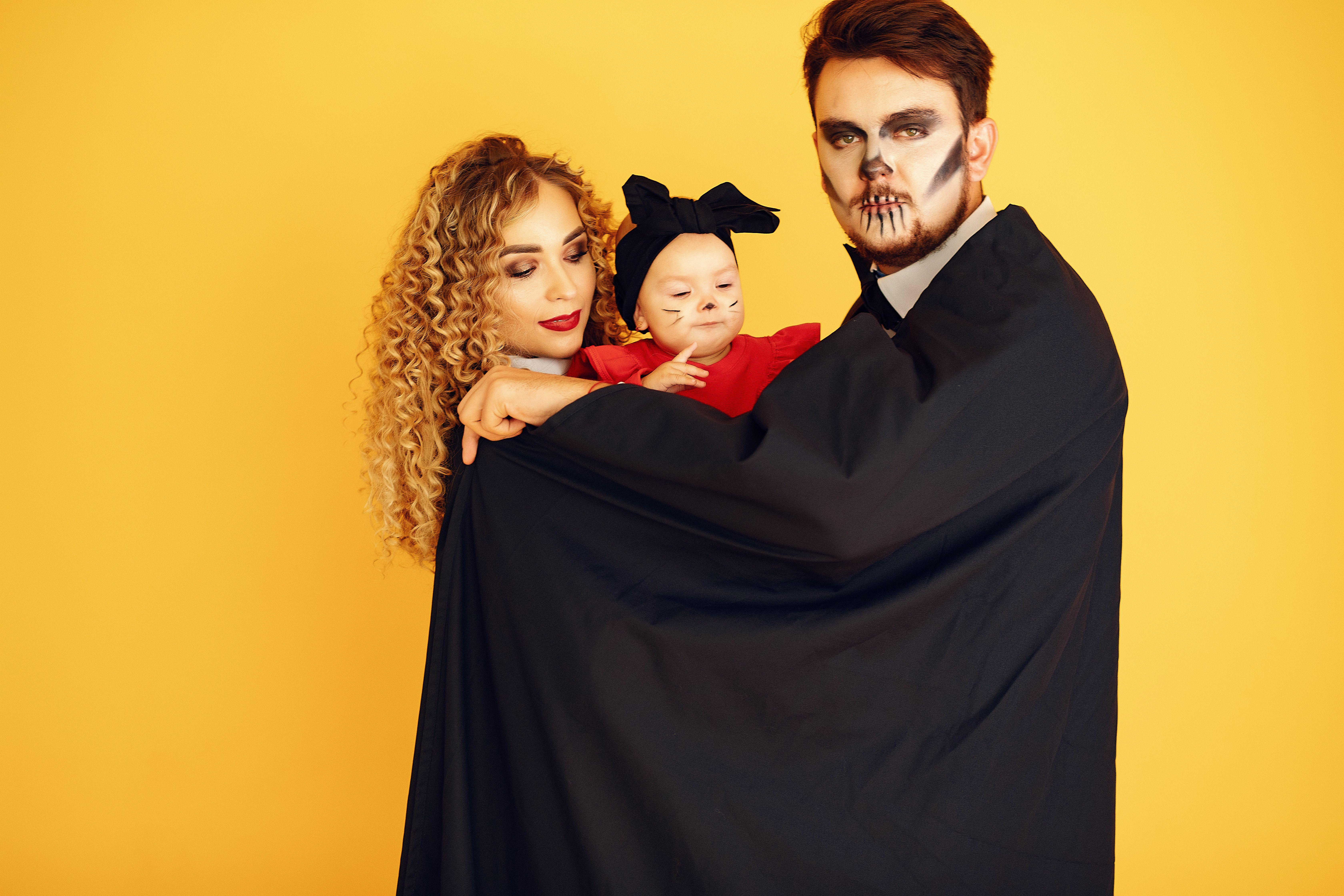A family of three dressed in Halloween costumes against a yellow background. Fun and spooky theme.