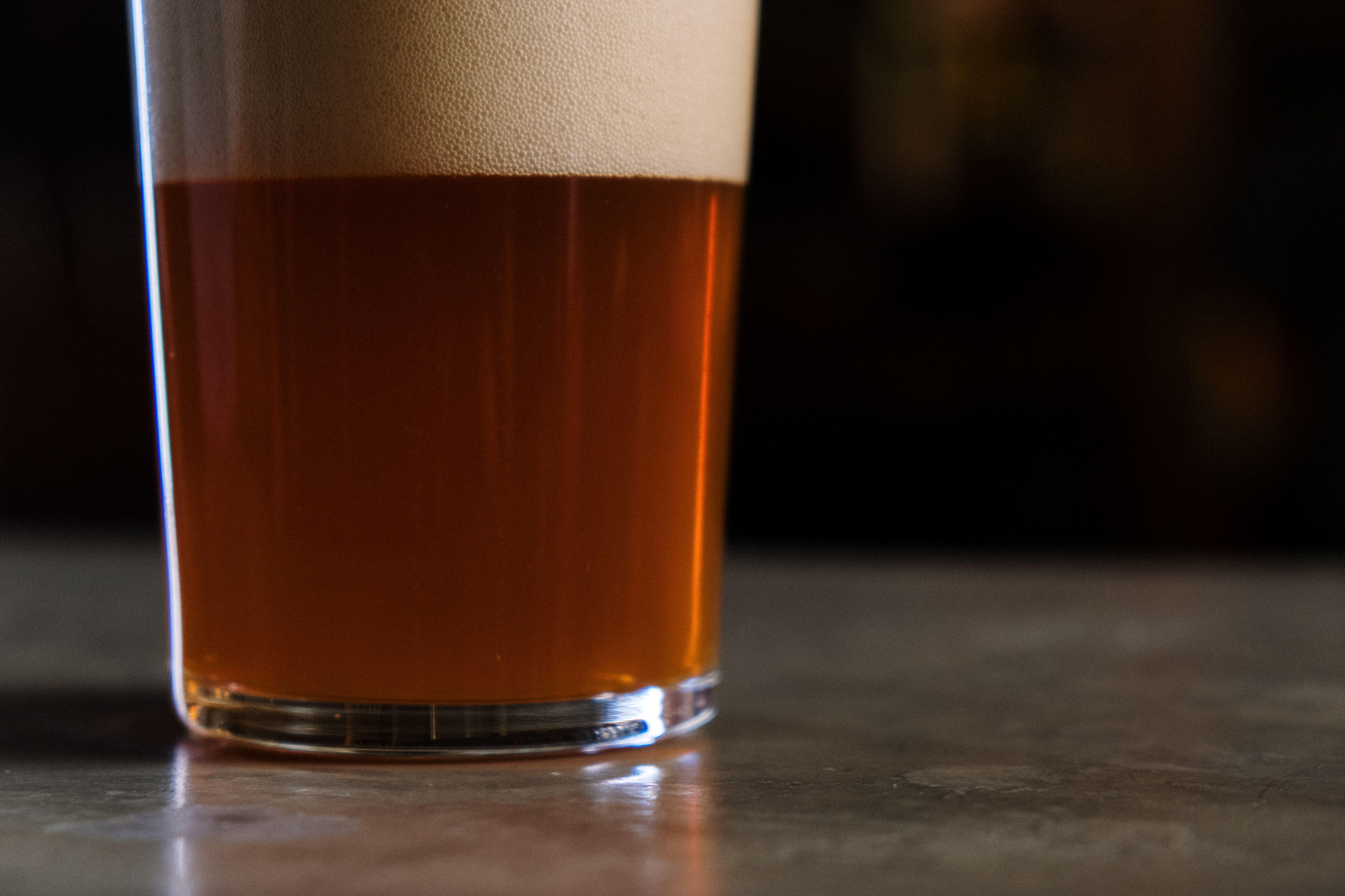 A detailed shot of a glass of amber craft beer topped with foam, set against a dark background.