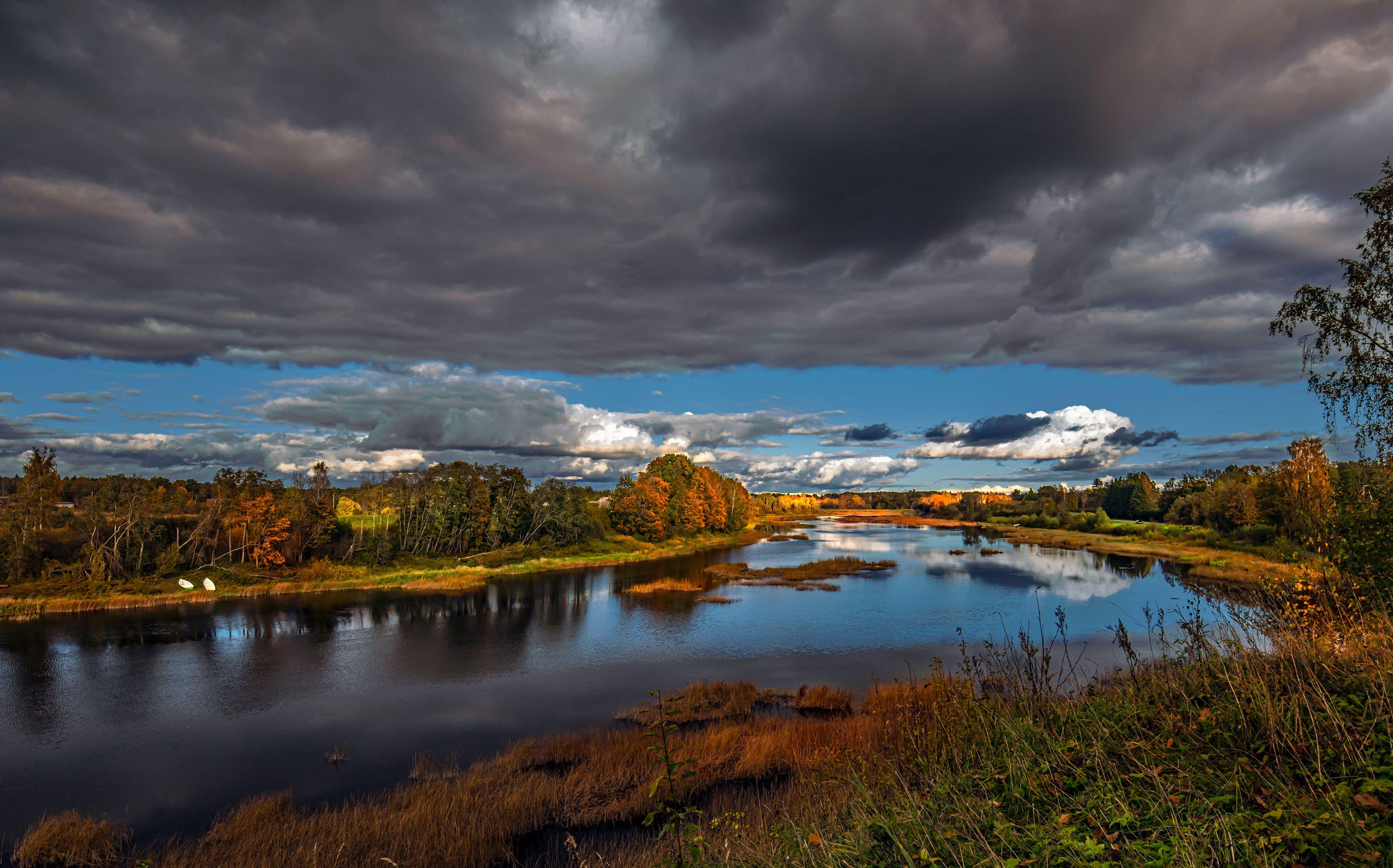 Stunning autumn view of Pärnu River with dark clouds and vibrant foliage in Estonia.