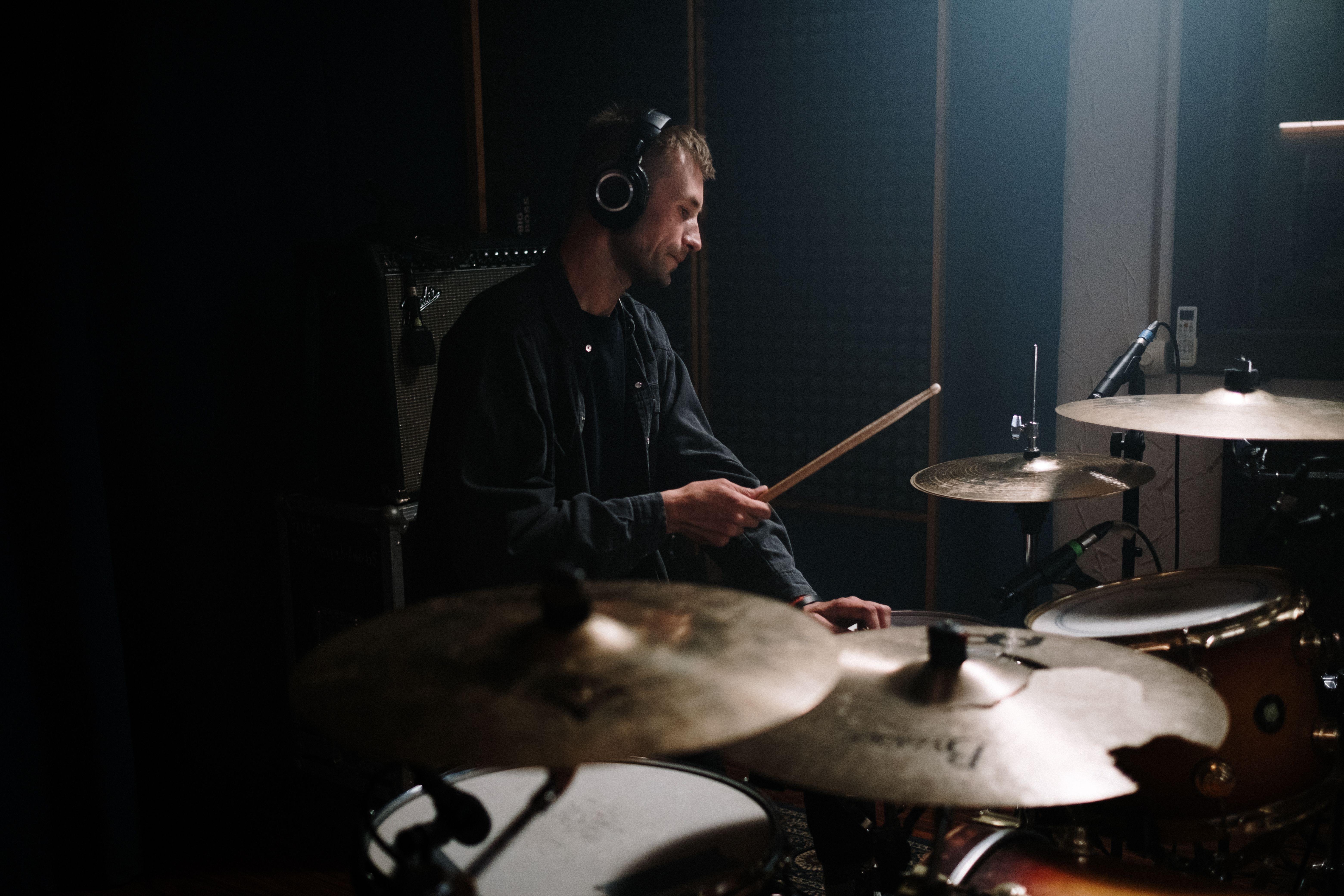 A man playing drums with headphones in a recording studio, perfect for music themes.