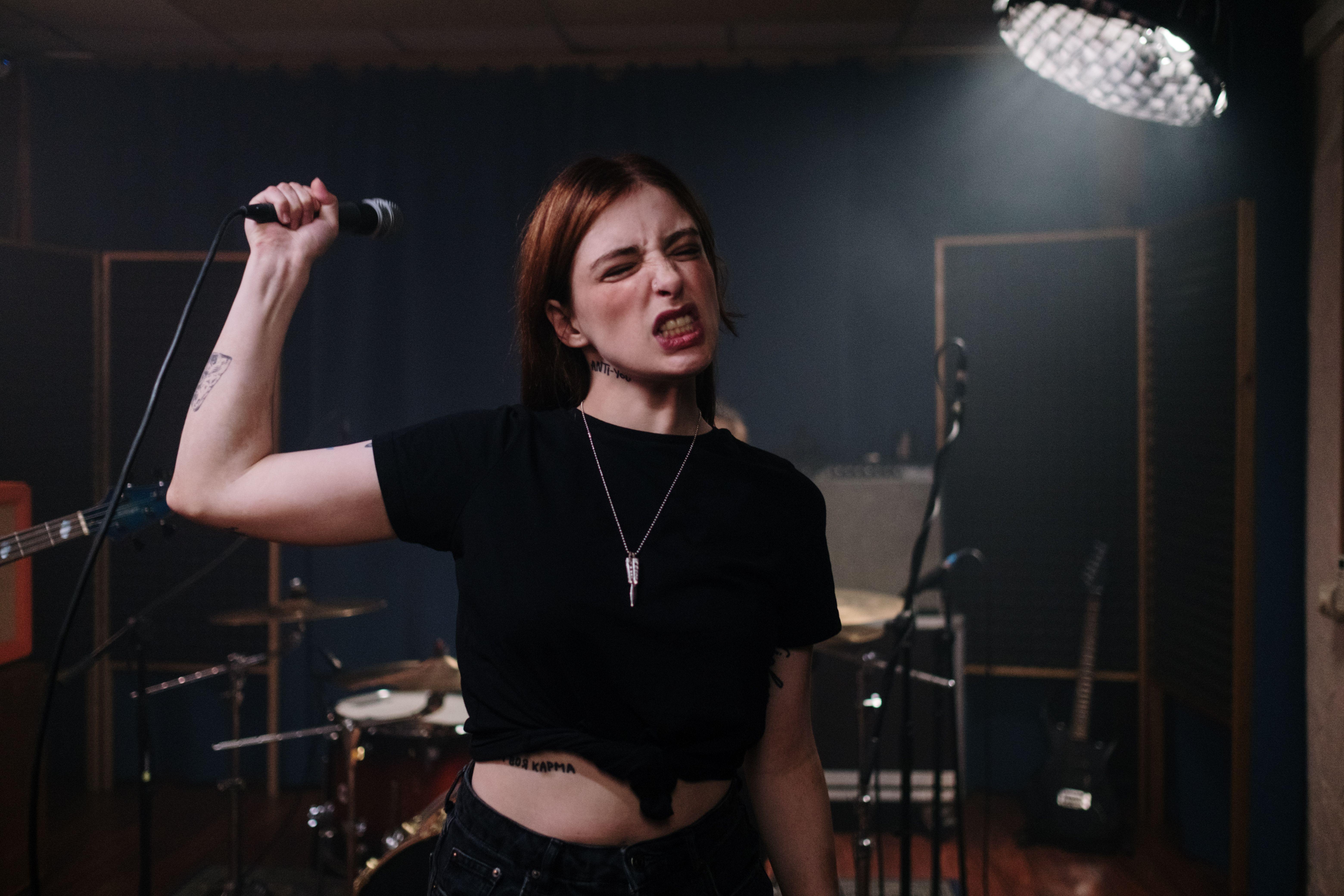Energetic female singer with microphone in music rehearsal studio, expressing emotion.