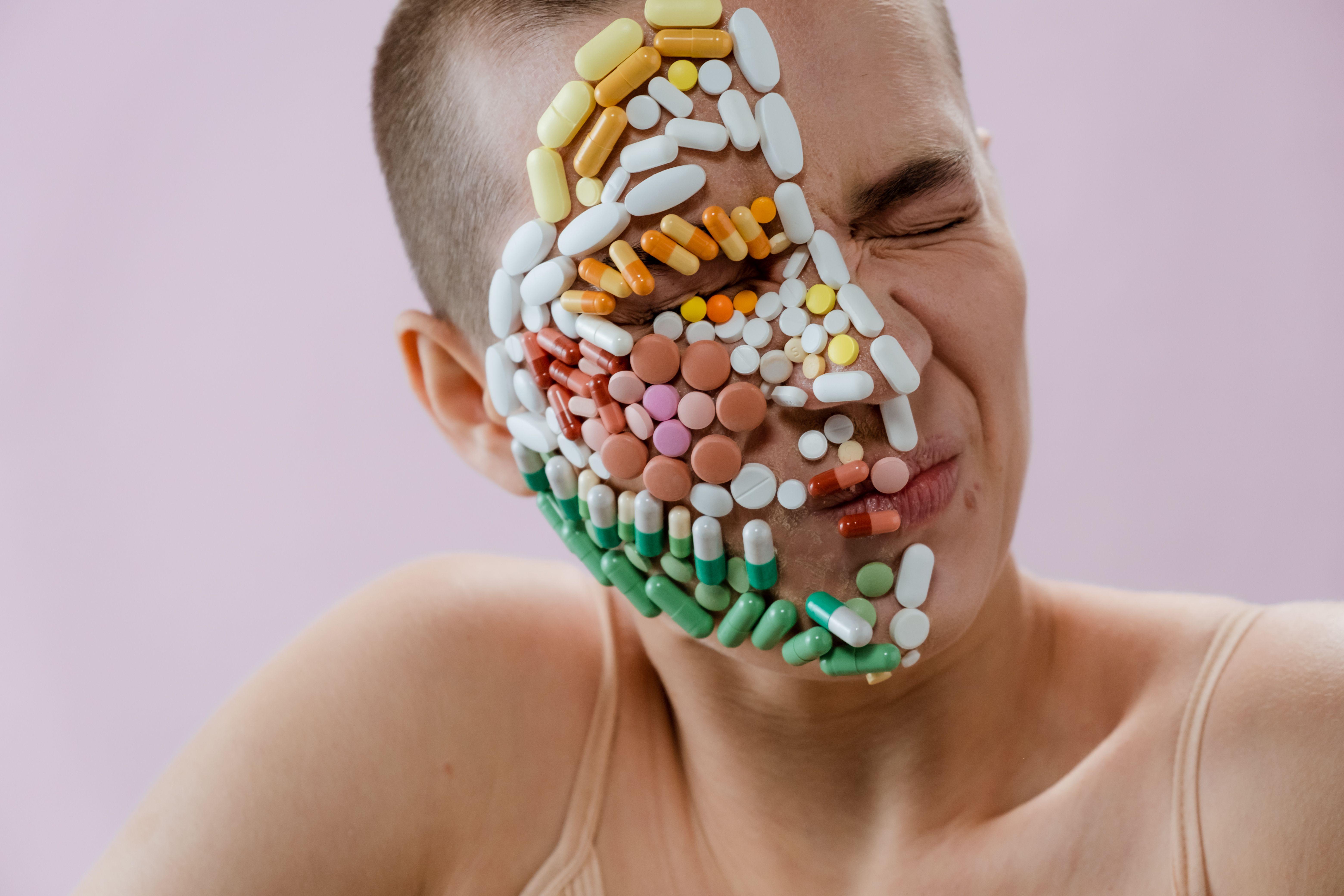Creative portrait of person with pills covering face, symbolizing medication dependence.