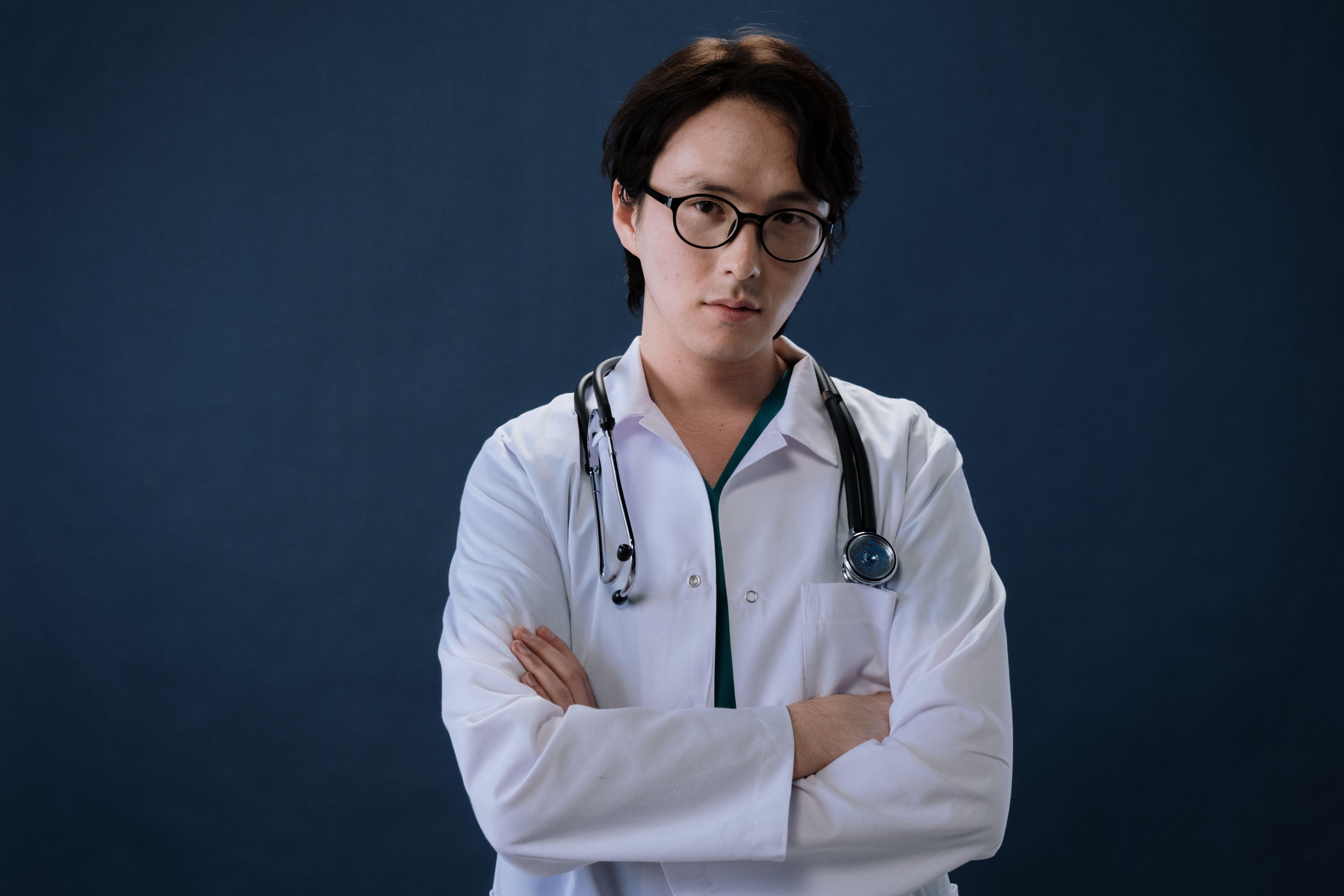 Portrait of a doctor with eyeglasses and stethoscope against a blue background in professional attire.