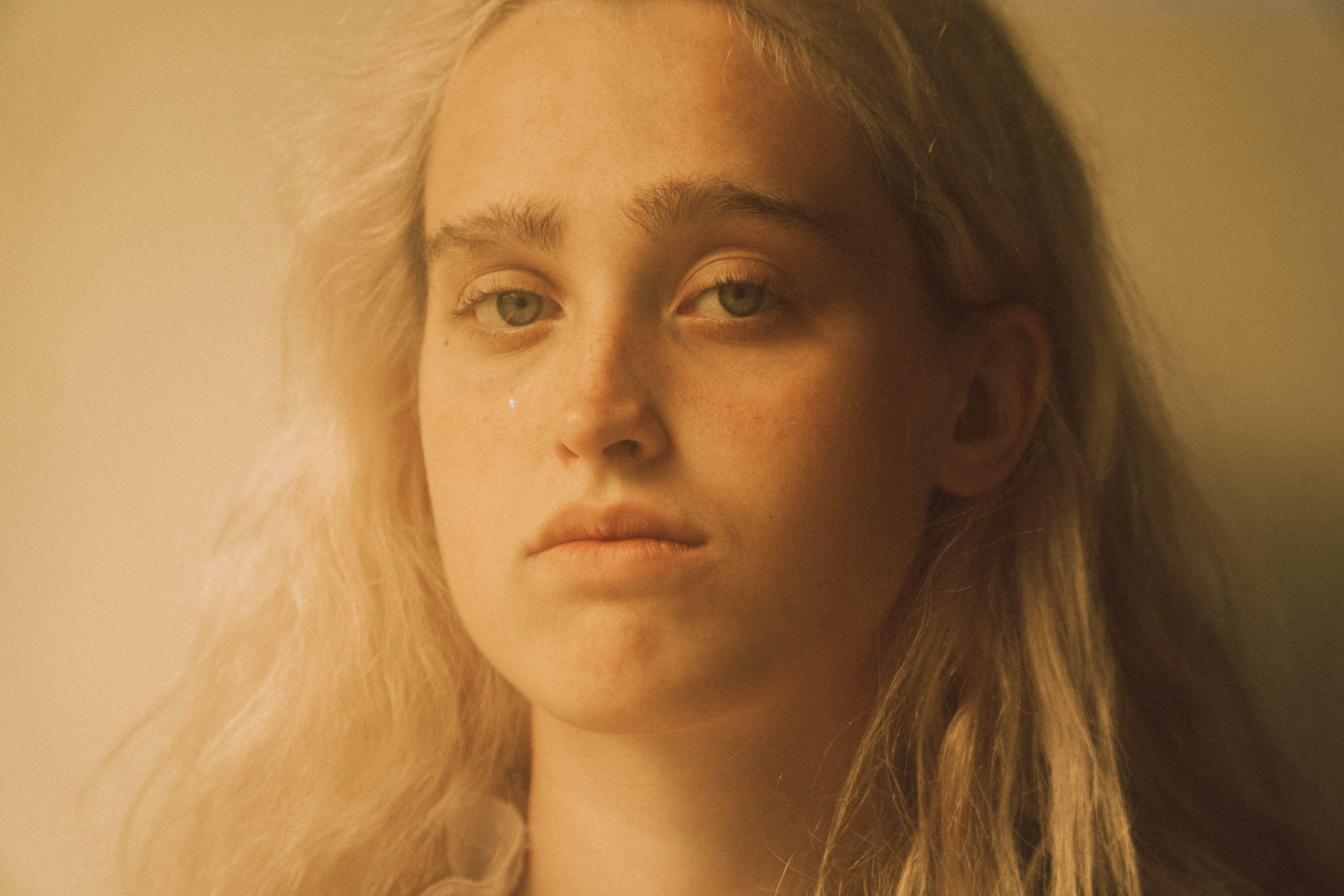Crop young sensitive female with blond hair and teardrop on cheek looking at camera