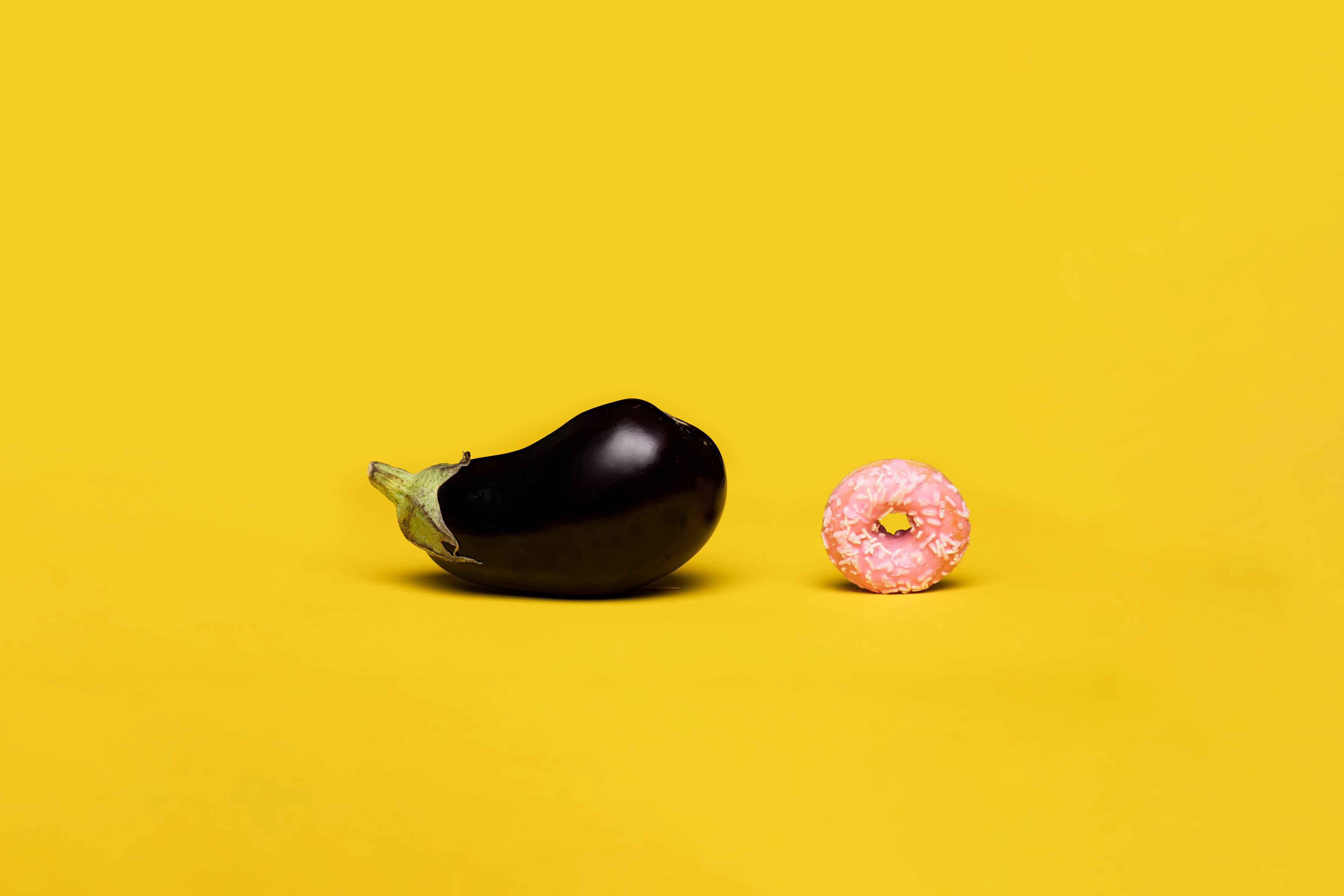 Vibrant conceptual art symbolizing sexual education using eggplant and donut on yellow background.