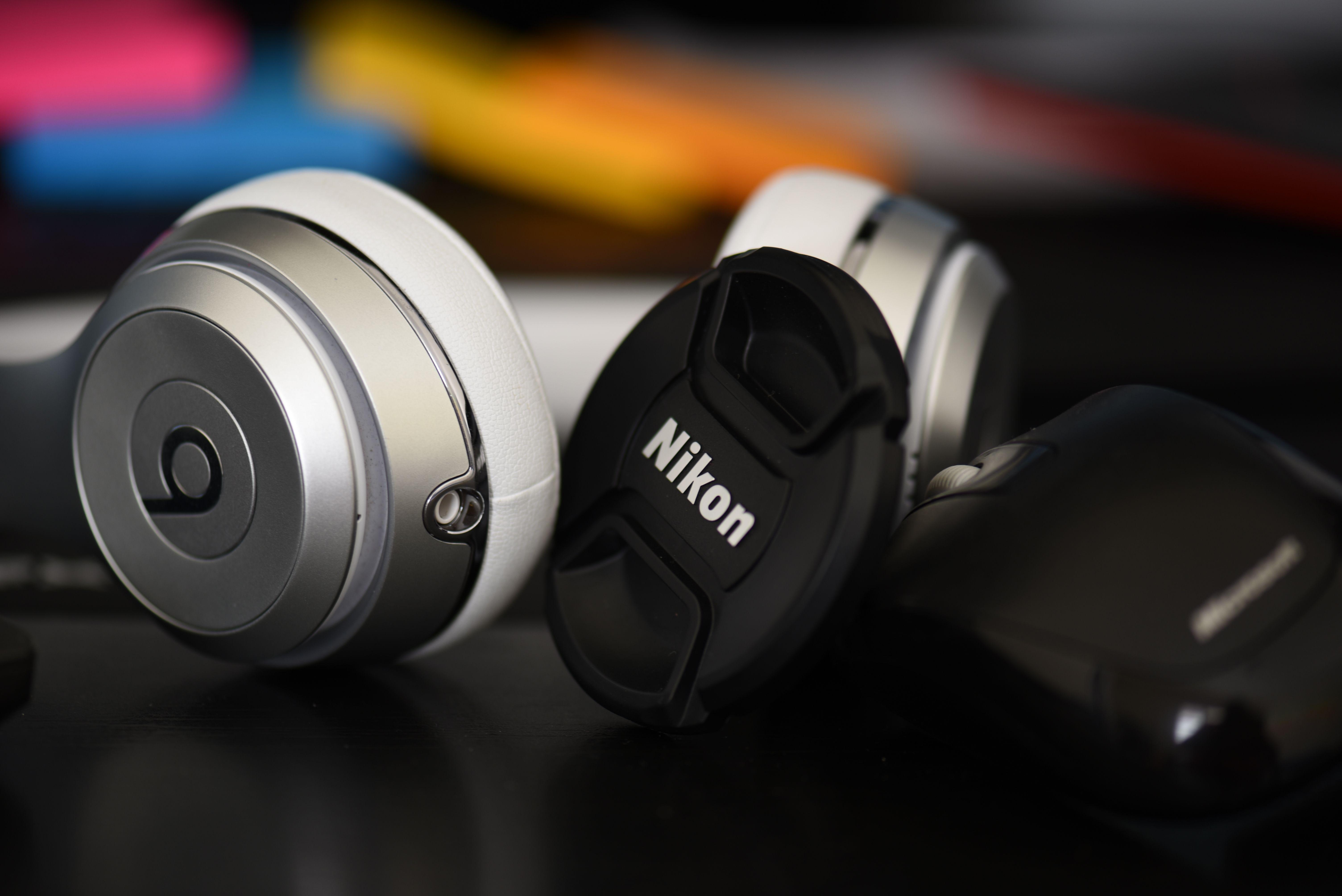 Detailed close-up of silver headphones and a Nikon lens cap on a dark surface.