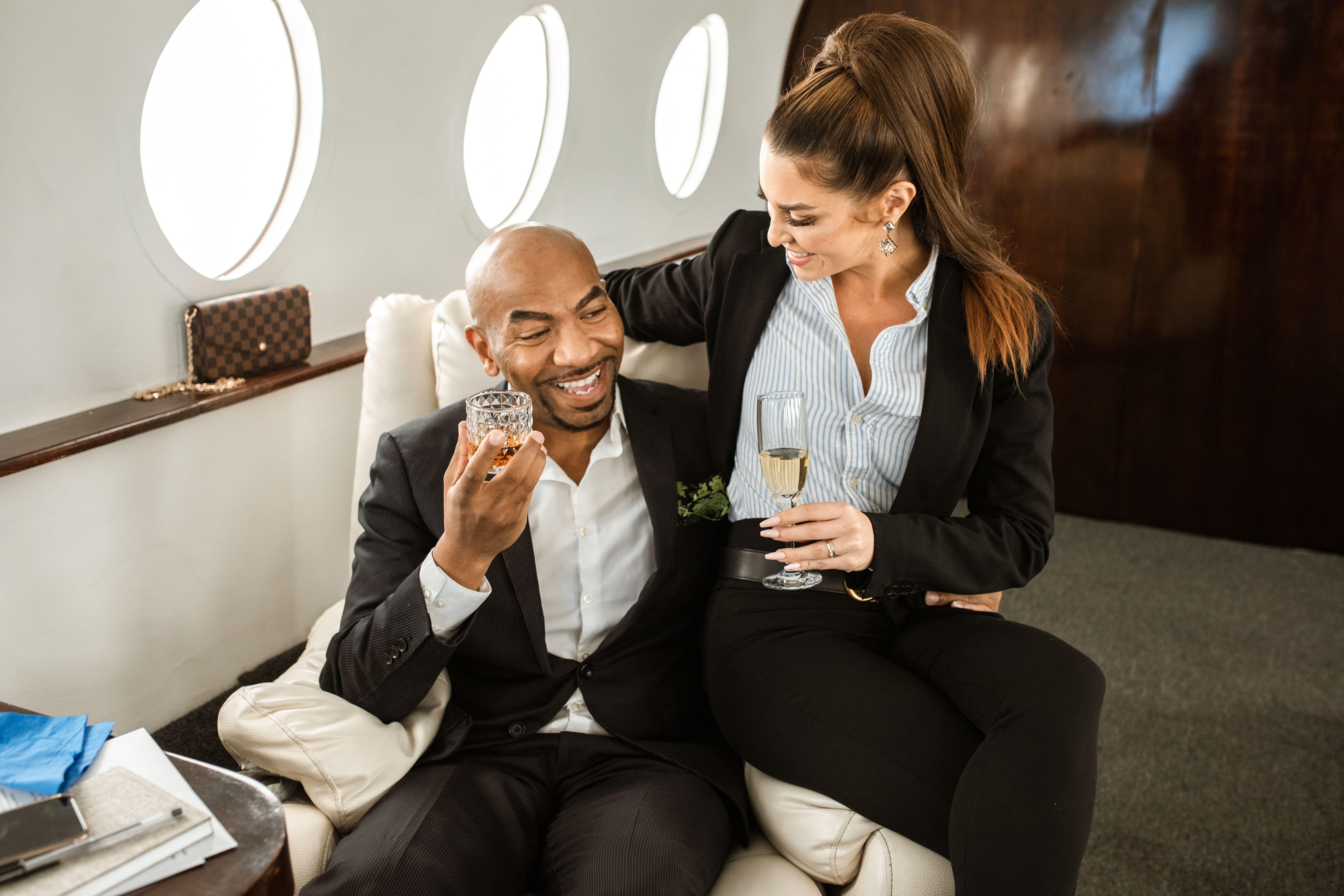 Couple in suits enjoying drinks in a private jet, symbolizing luxury and elegance.
