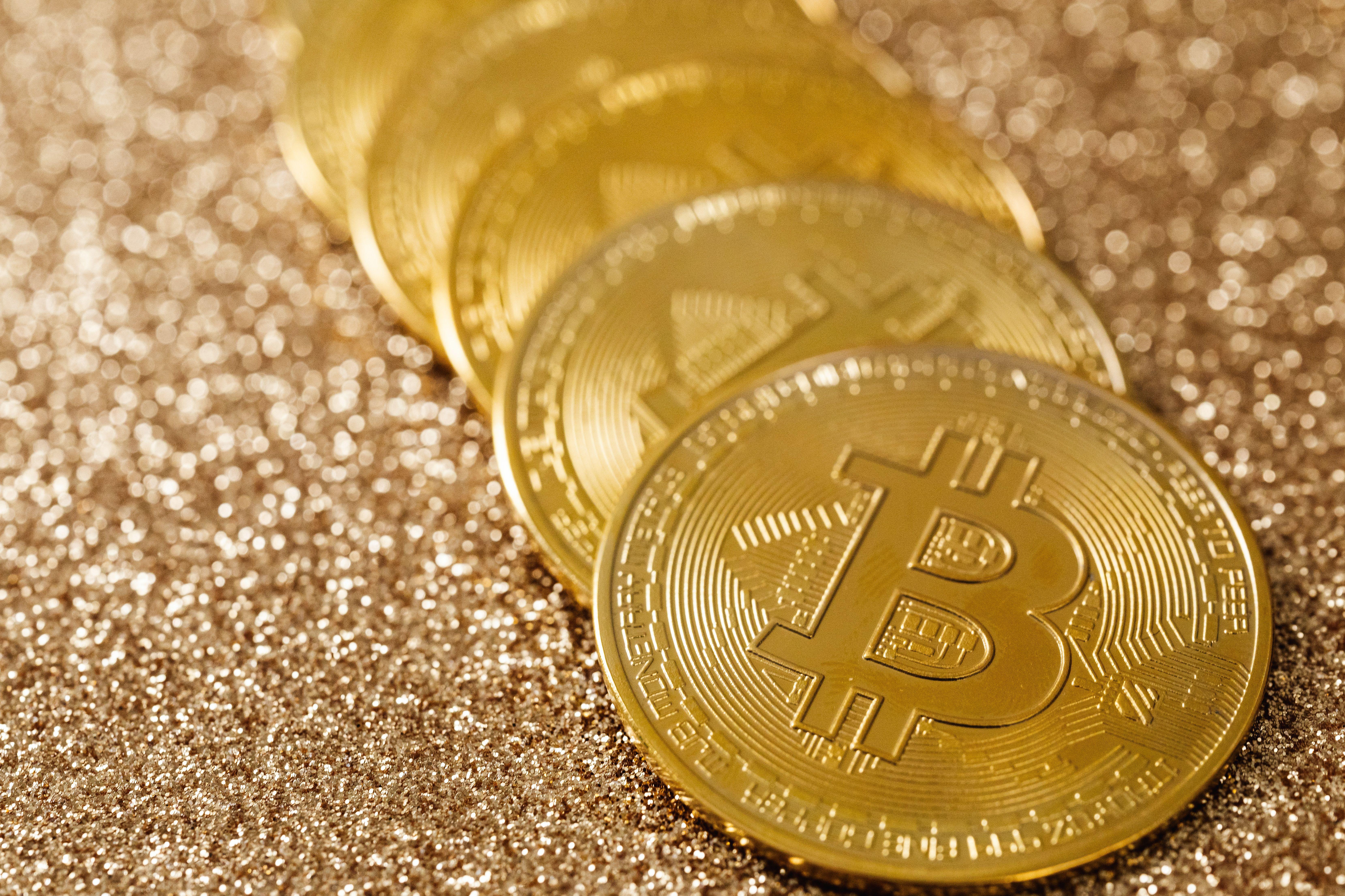 Close-up of golden Bitcoin coins on a shimmering glitter background, symbolizing digital currency's allure.