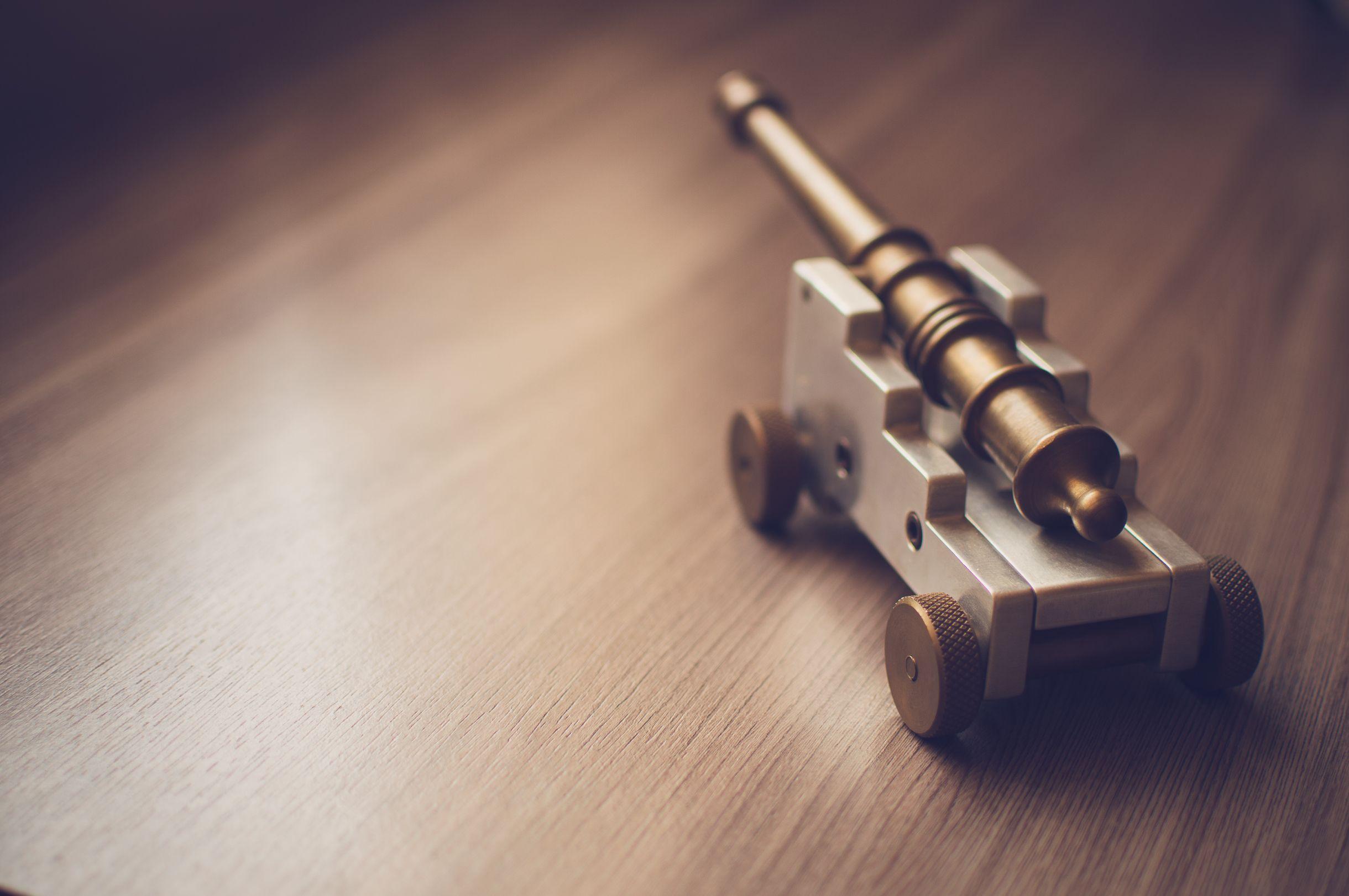 Close-up of a brass and silver miniature cannon toy placed on a wooden table.