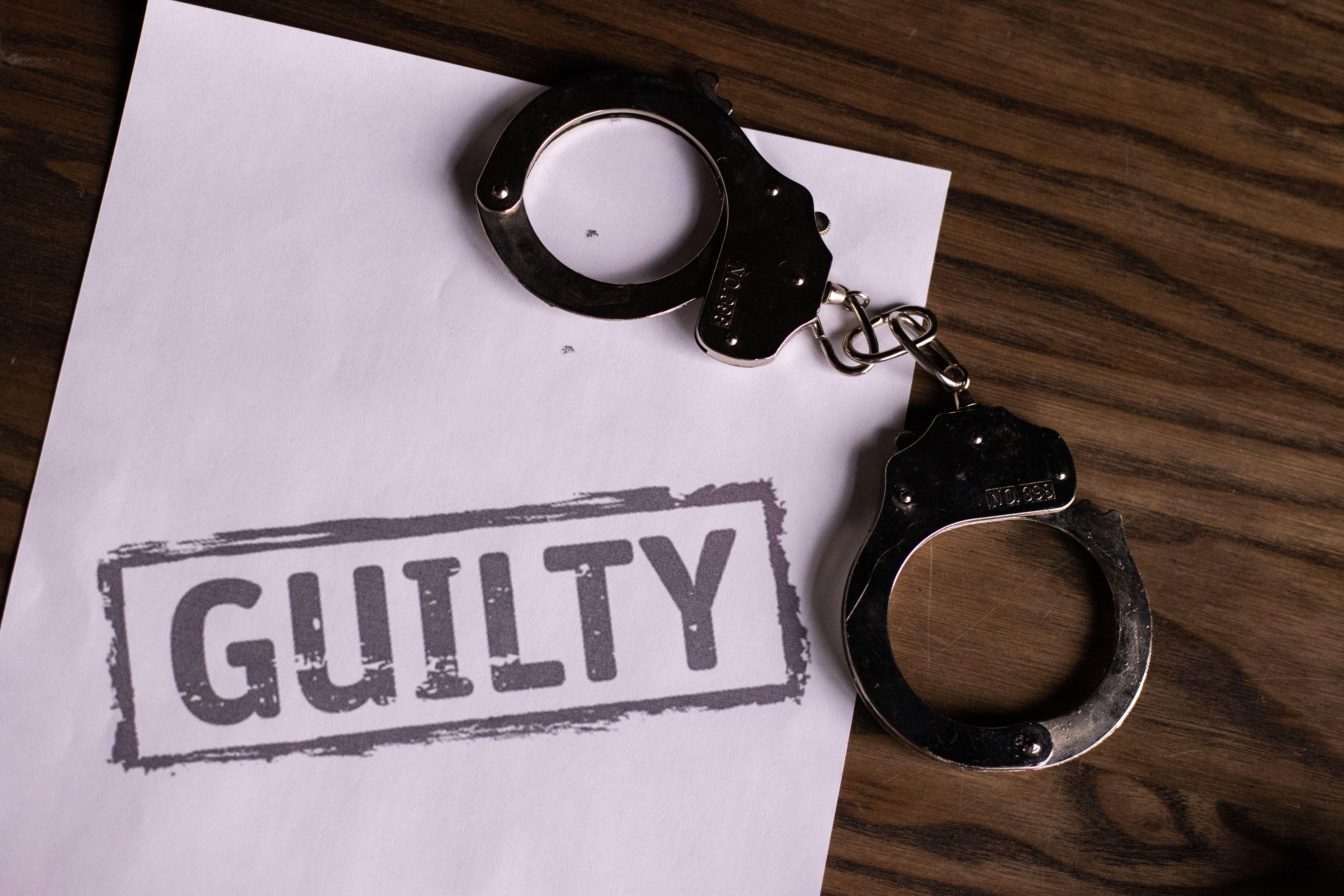 Top view of handcuffs on paper with 'GUILTY' text, symbolizing a verdict or crime.
