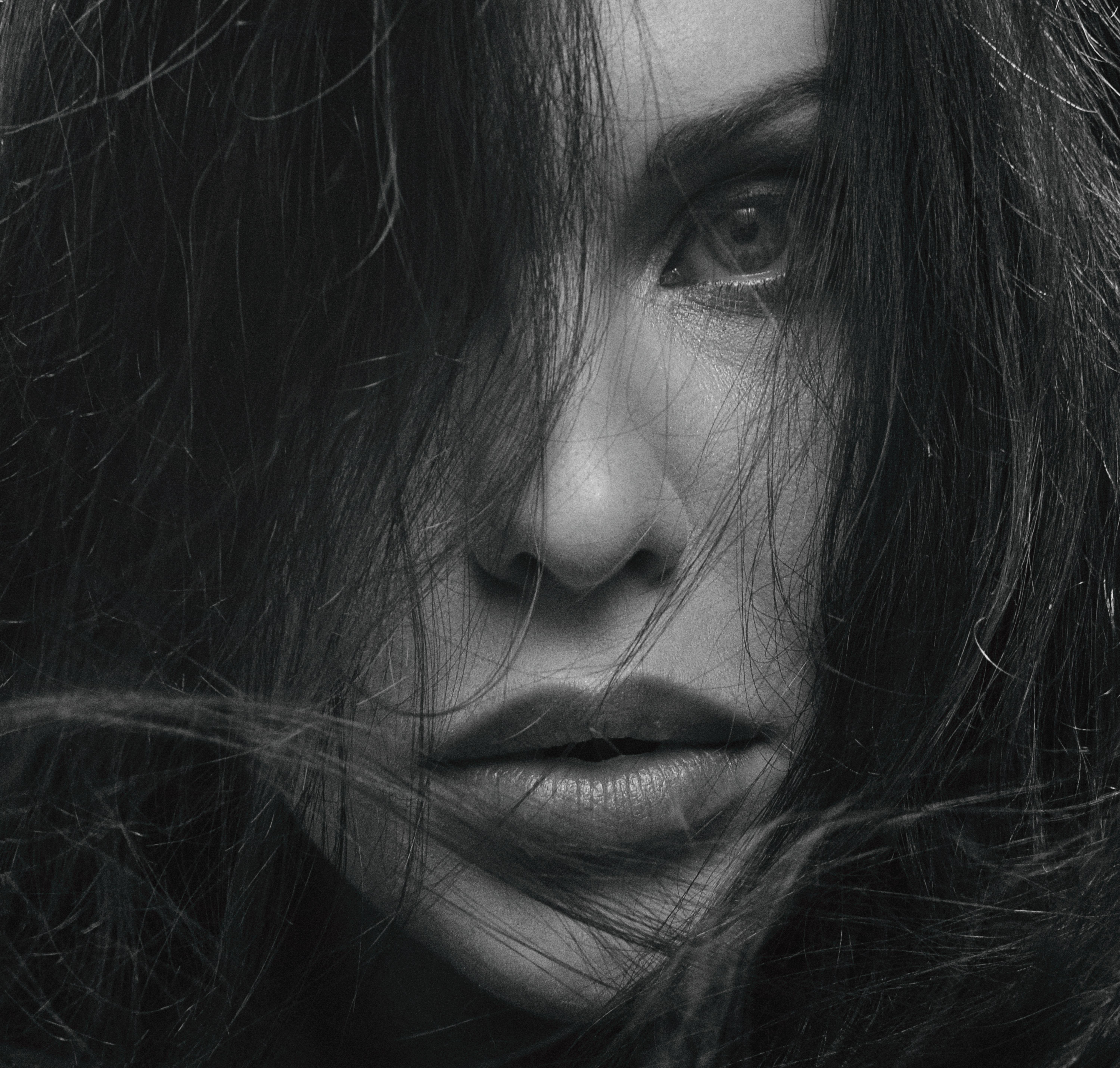 Striking grayscale close-up of a woman's face with hair framing her intense gaze.