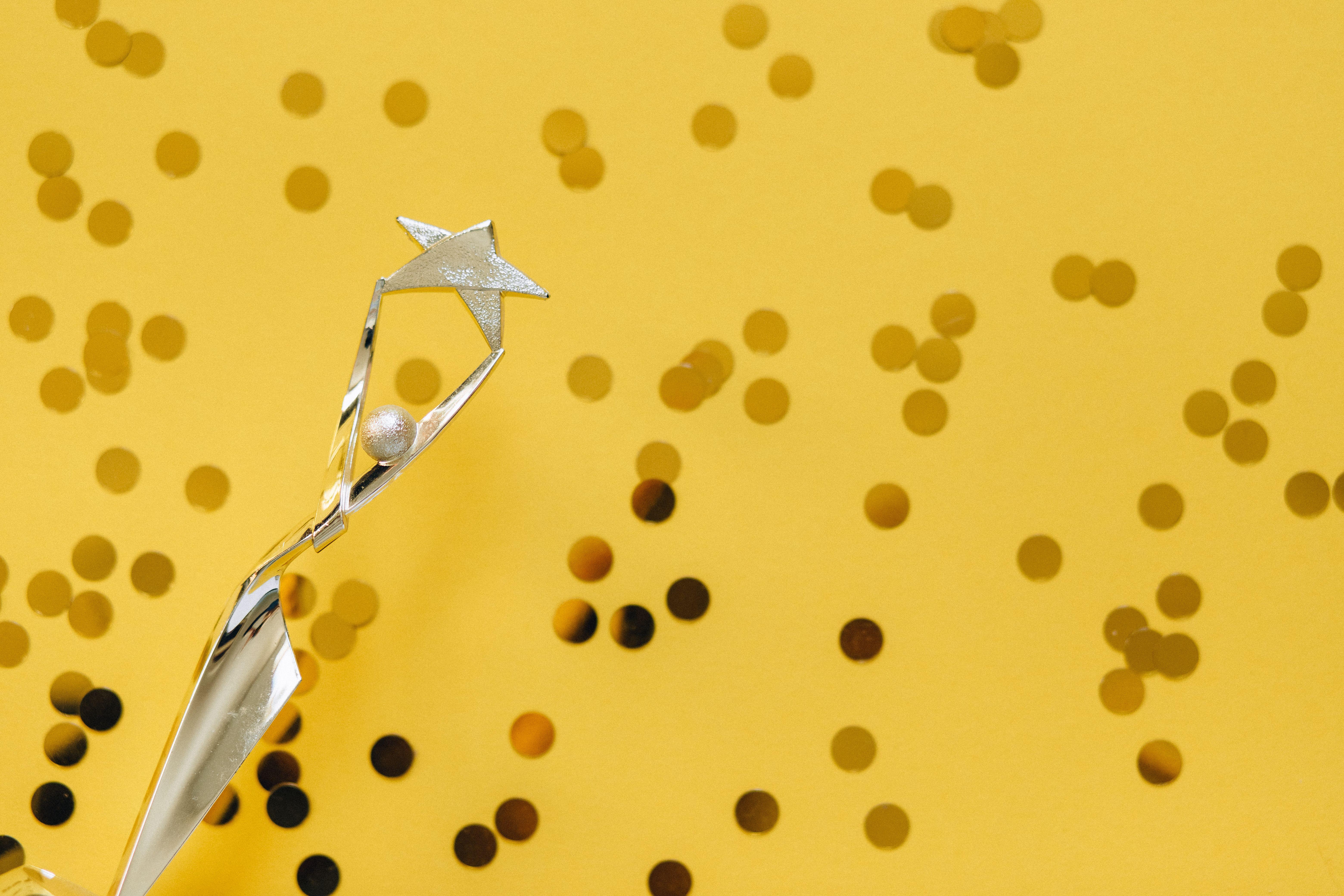 A silver trophy with a star design on a vibrant yellow background adorned with confetti.