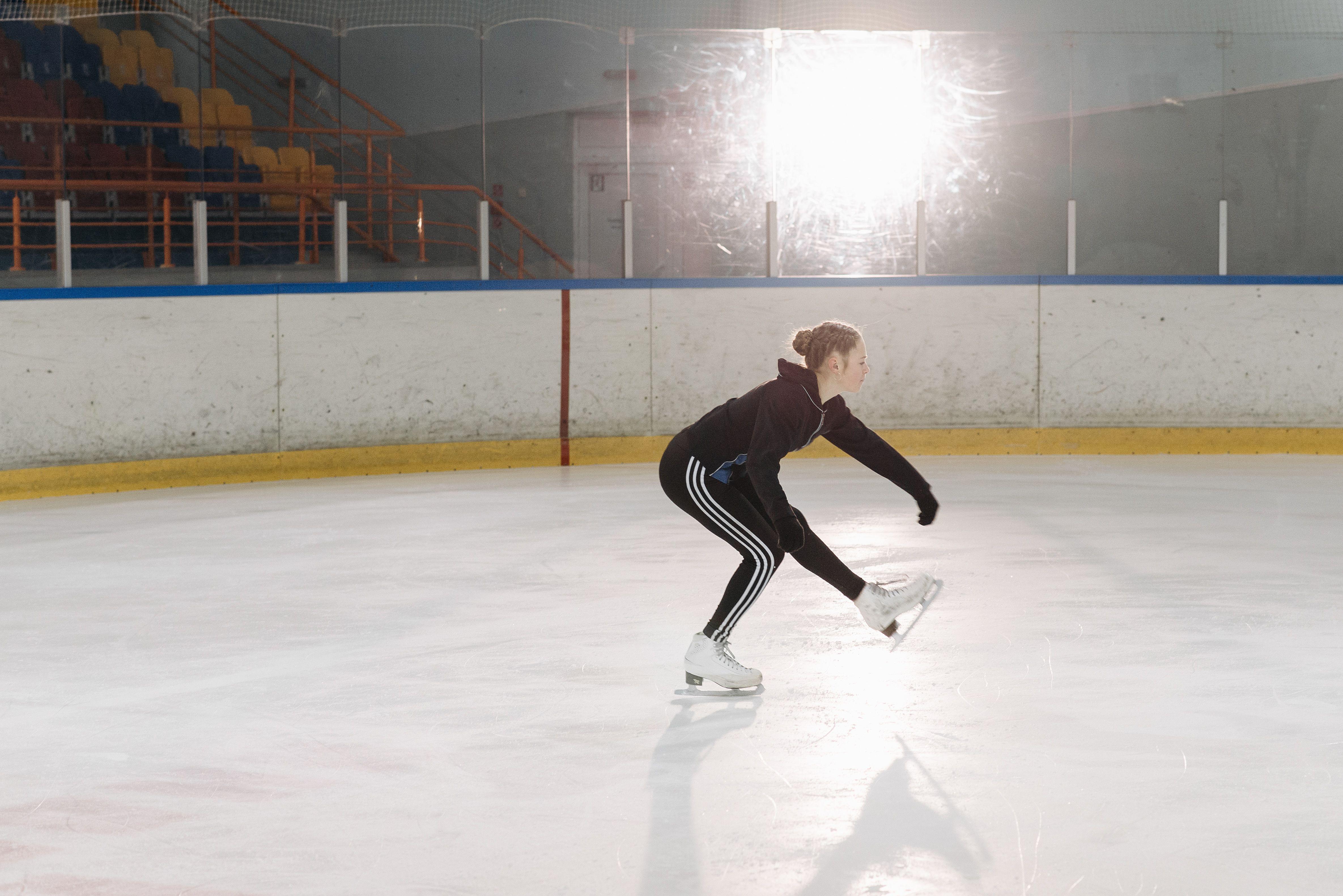 Young figure skater skillfully executes a sit spin on an indoor ice rink.
