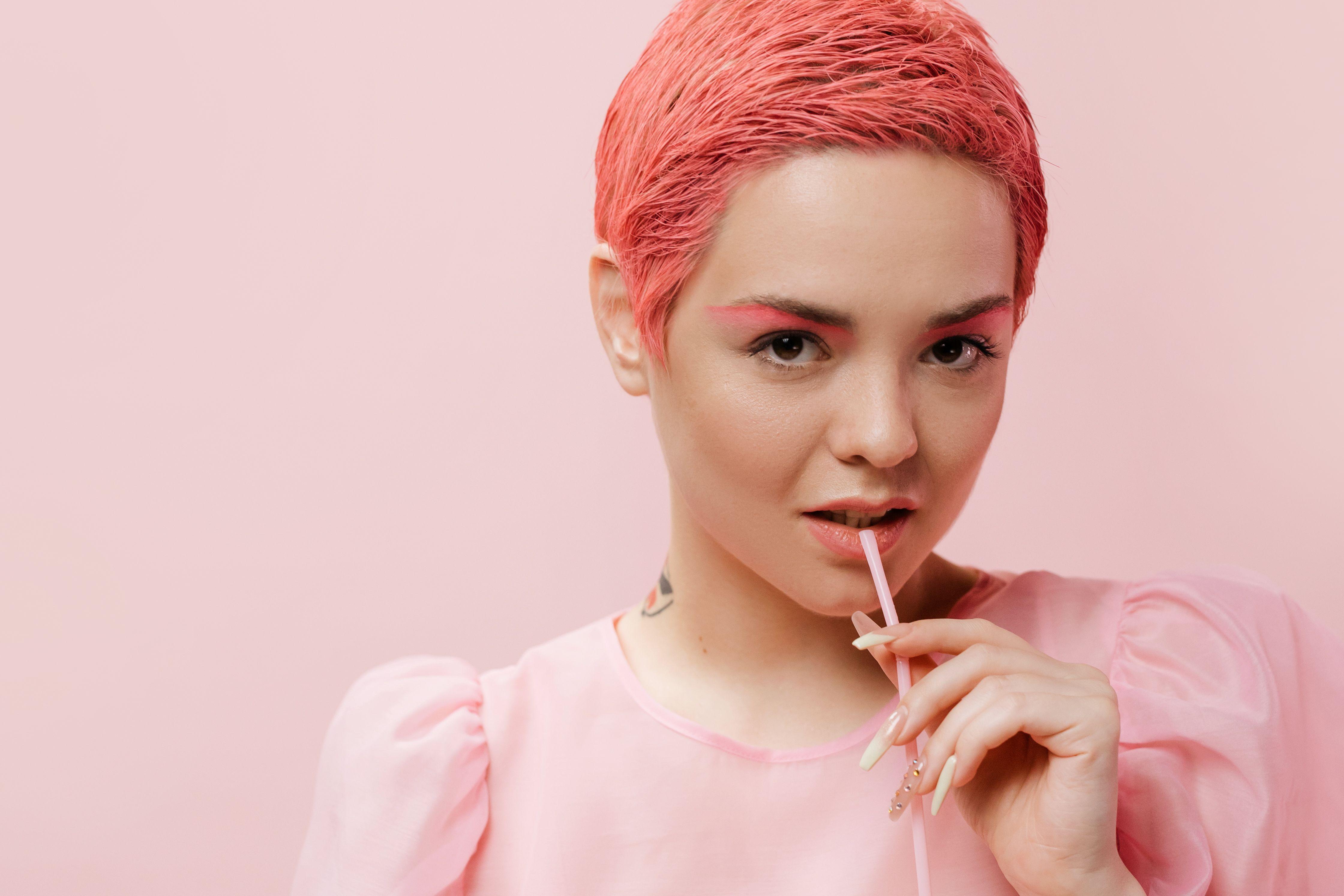 A trendy young woman with pink hair poses confidently in a studio setting, showcasing modern fashion.