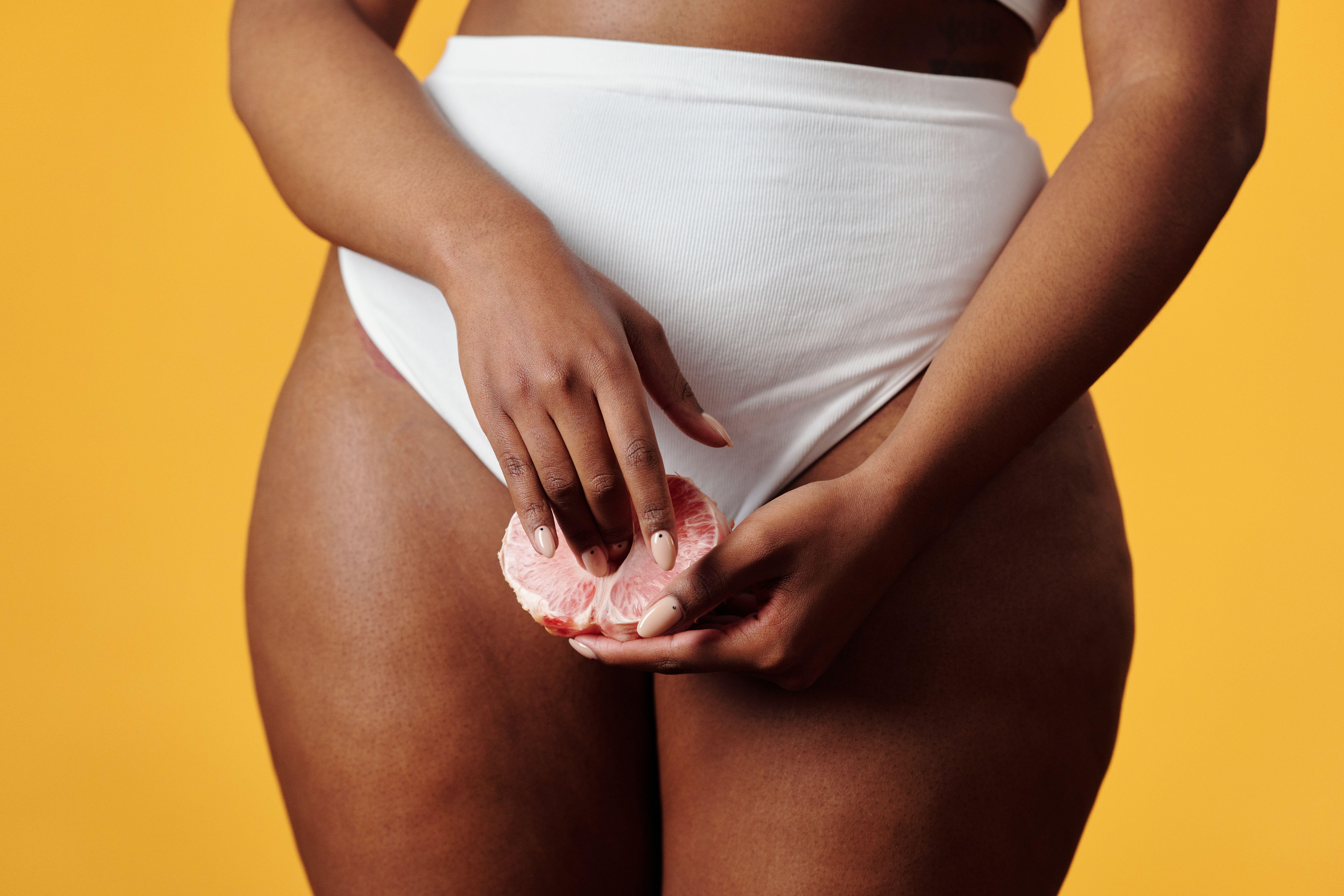 A woman in white underwear holds a pomelo slice against a vibrant yellow backdrop, showcasing fruit and fashion.