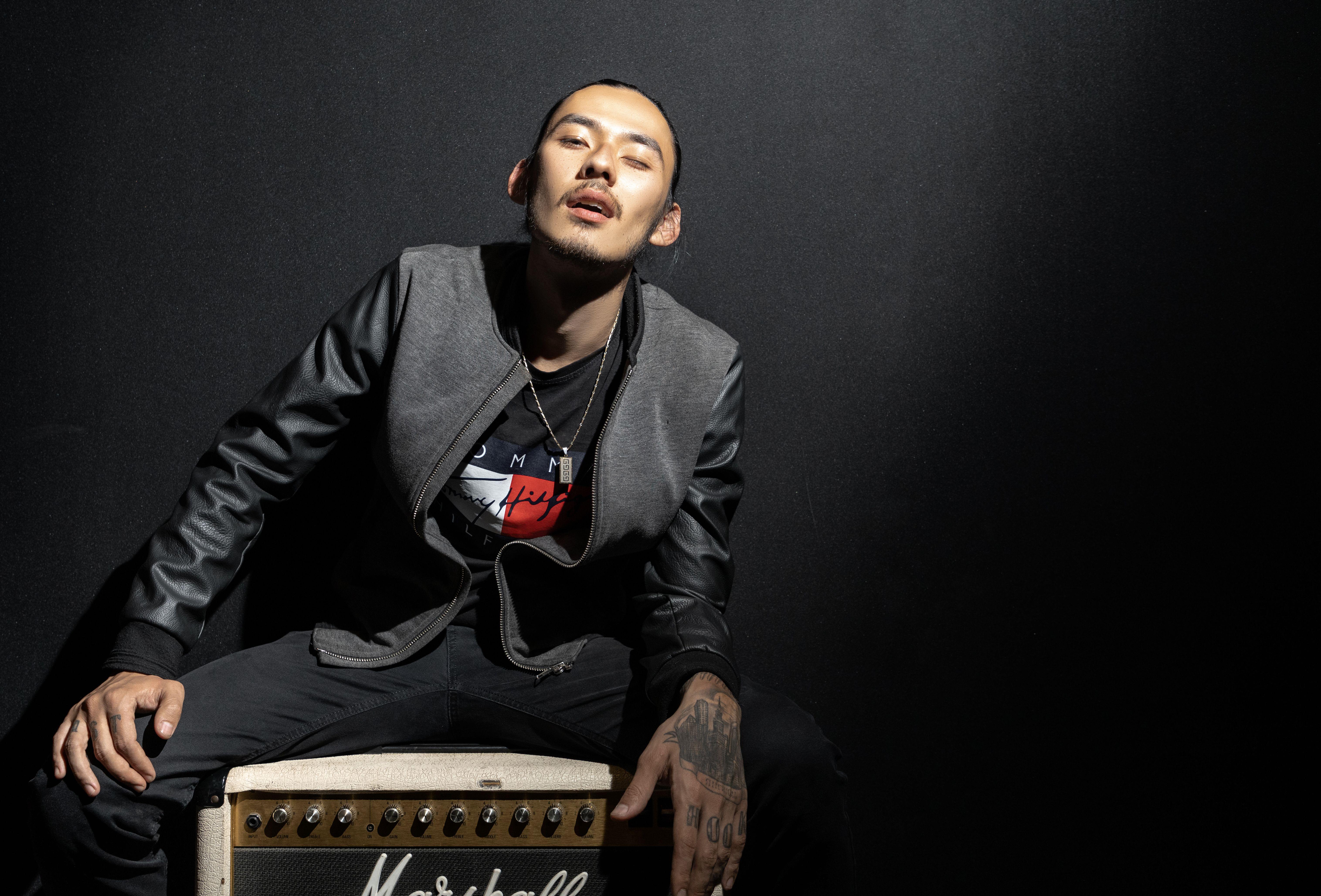 Stylish man in leather jacket poses confidently with amplifier in a studio setting.