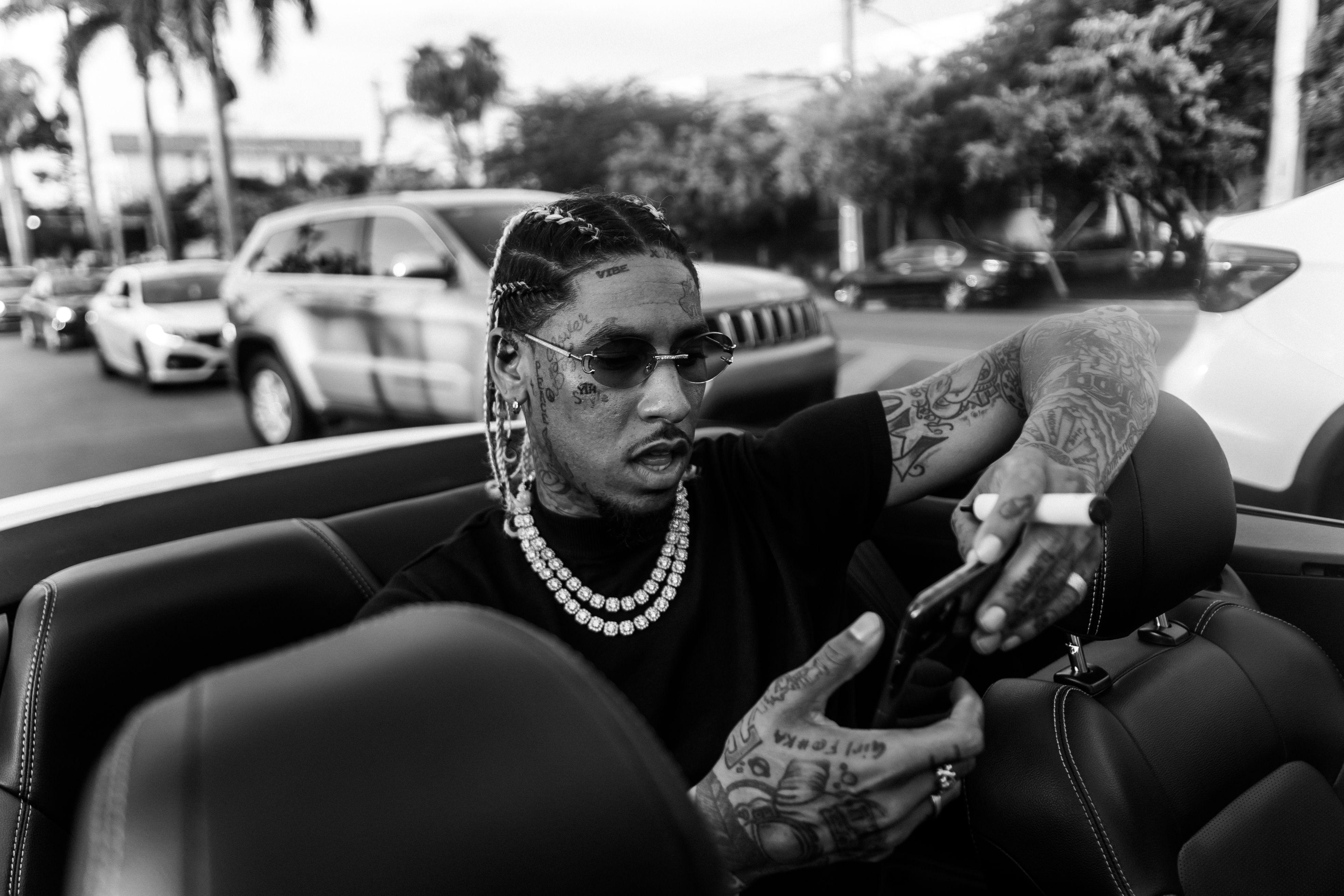 Black and white of African American tattooed male looking at mobile phone in sunglasses with dreadlocks and beads on neck