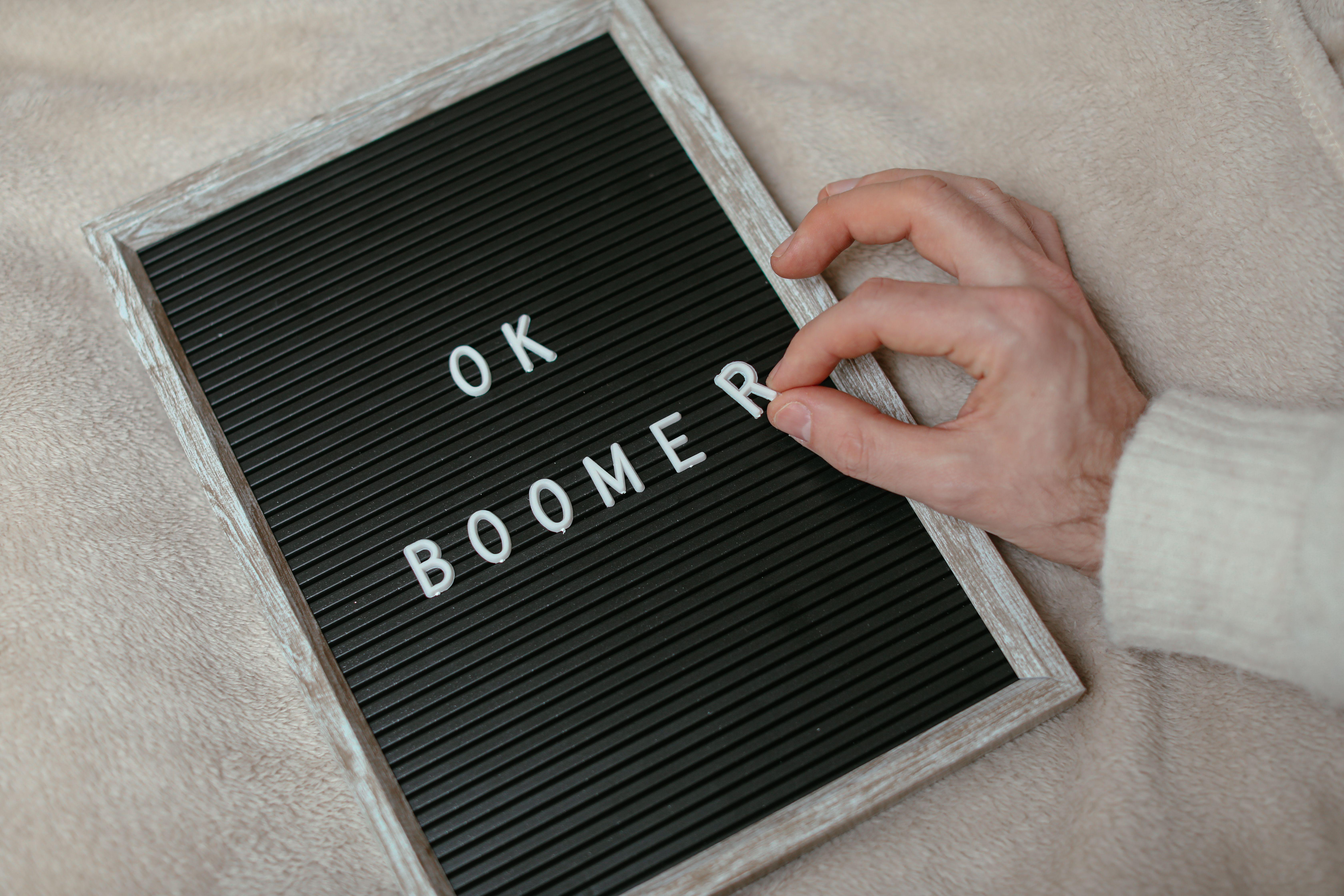 A close-up of a hand arranging letters to spell 'OK Boomer' on a felt letter board.