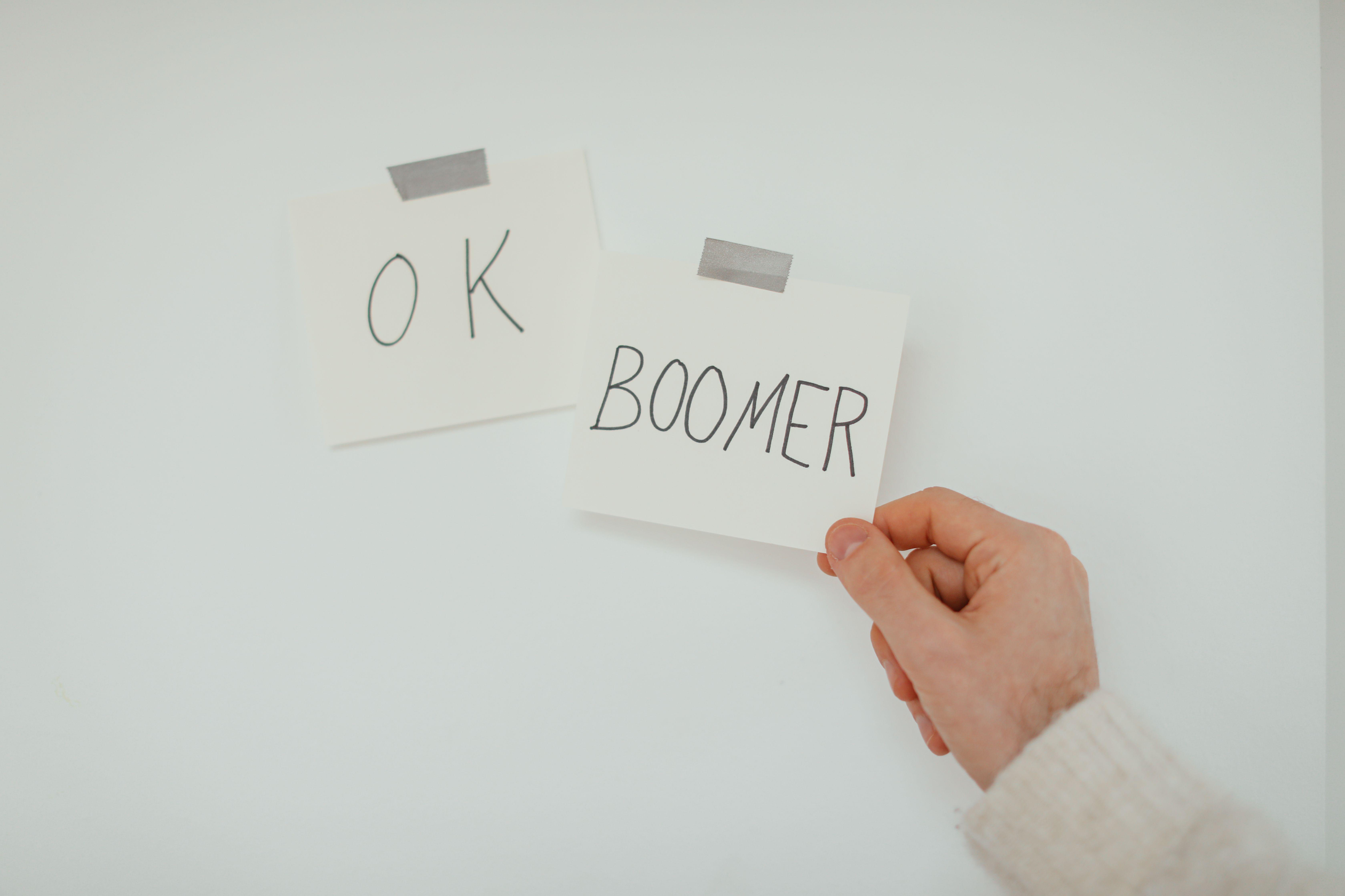 A hand holding a sticky note with the popular phrase 'OK Boomer', illustrating generational dialogue.