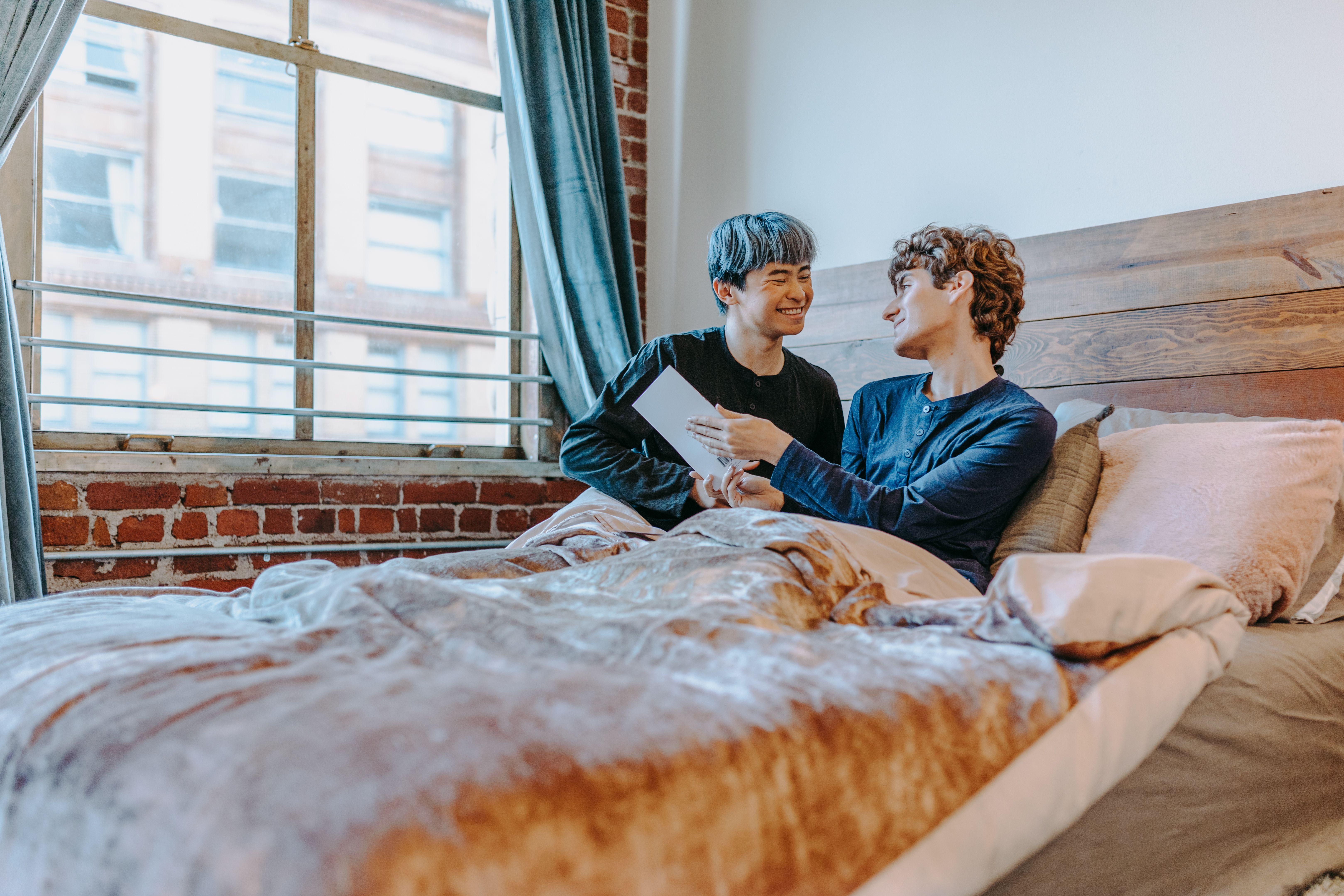 Two smiling adults in a cozy bedroom setting, sharing an intimate and joyful moment.