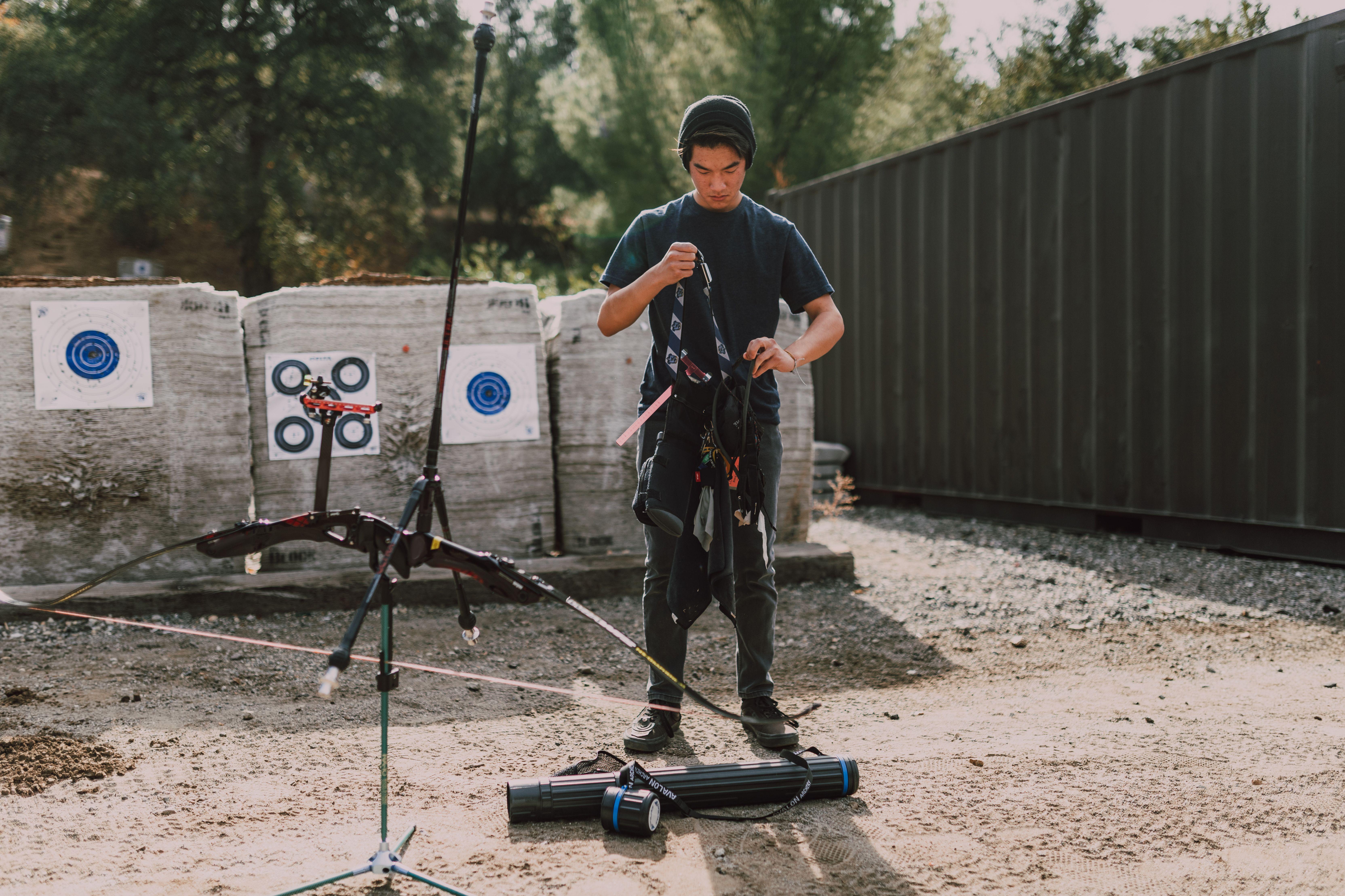 Teen adjusting equipment at an outdoor archery range, a focus on youth archery practice.