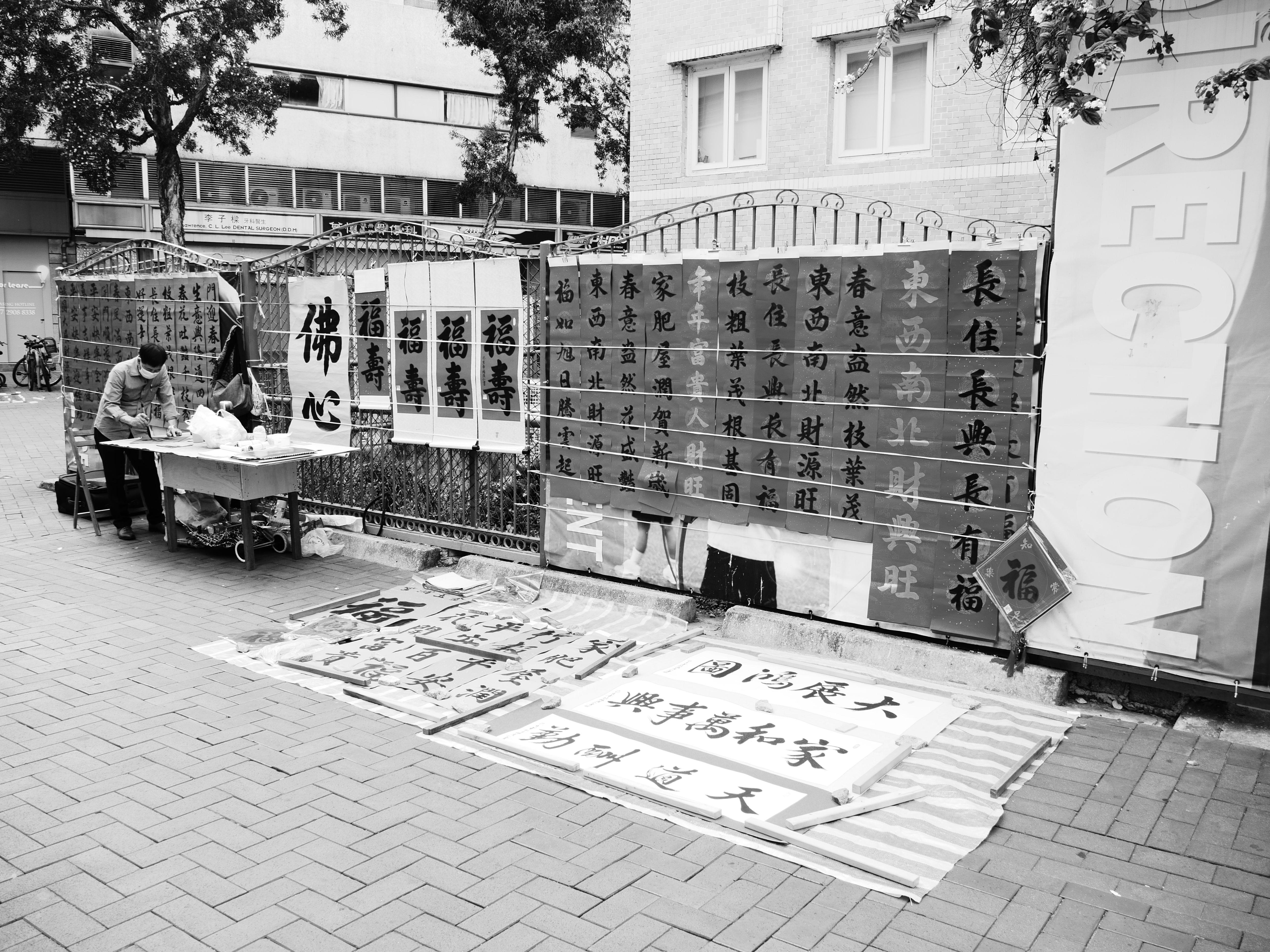 Grayscale photo of a street calligraphy stall in Hong Kong, showcasing Chinese characters.