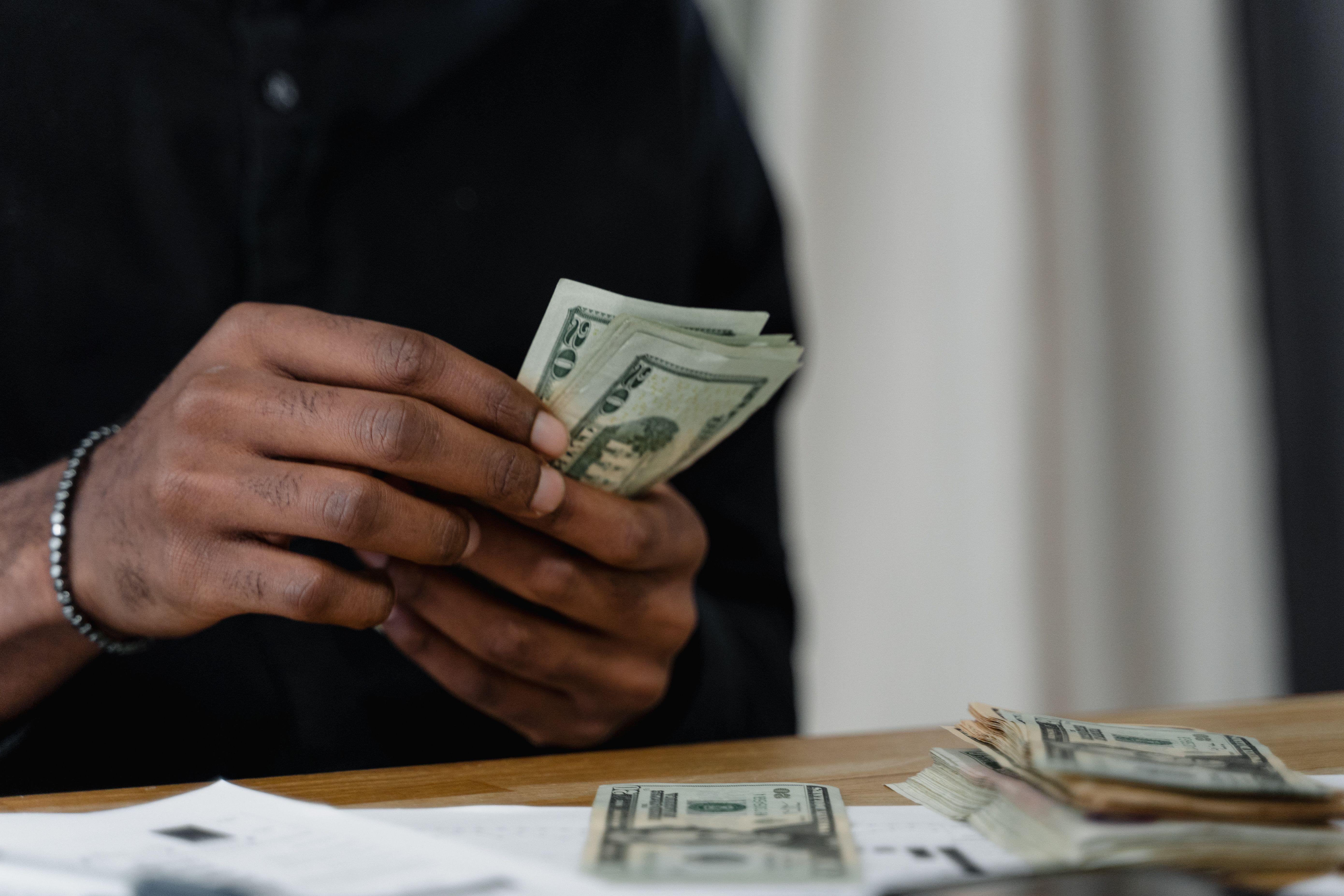 Adult counting dollar bills at a desk, focused on money management and finance.