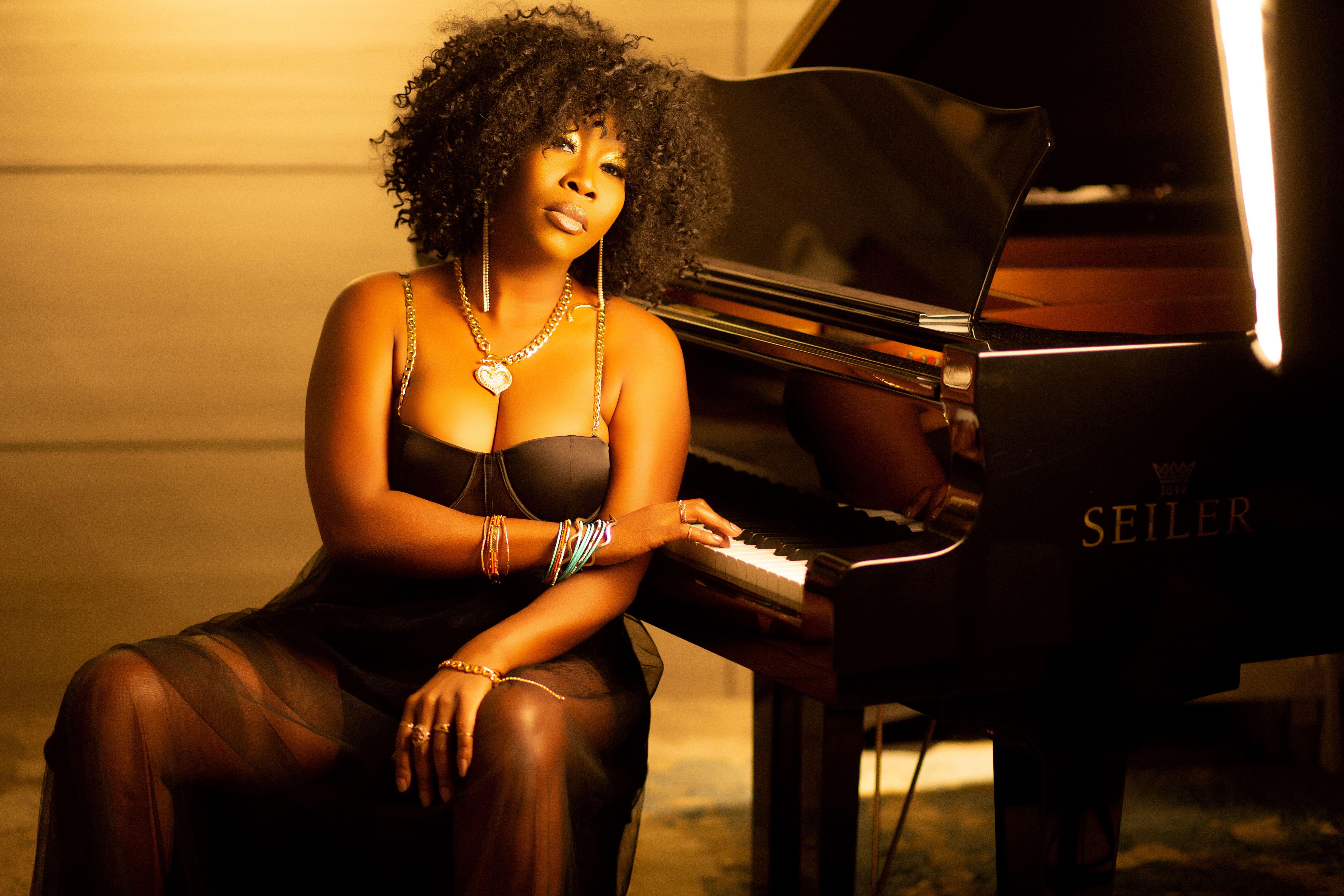 Woman with afro hair sitting at a grand piano in warm lighting, exuding elegance.