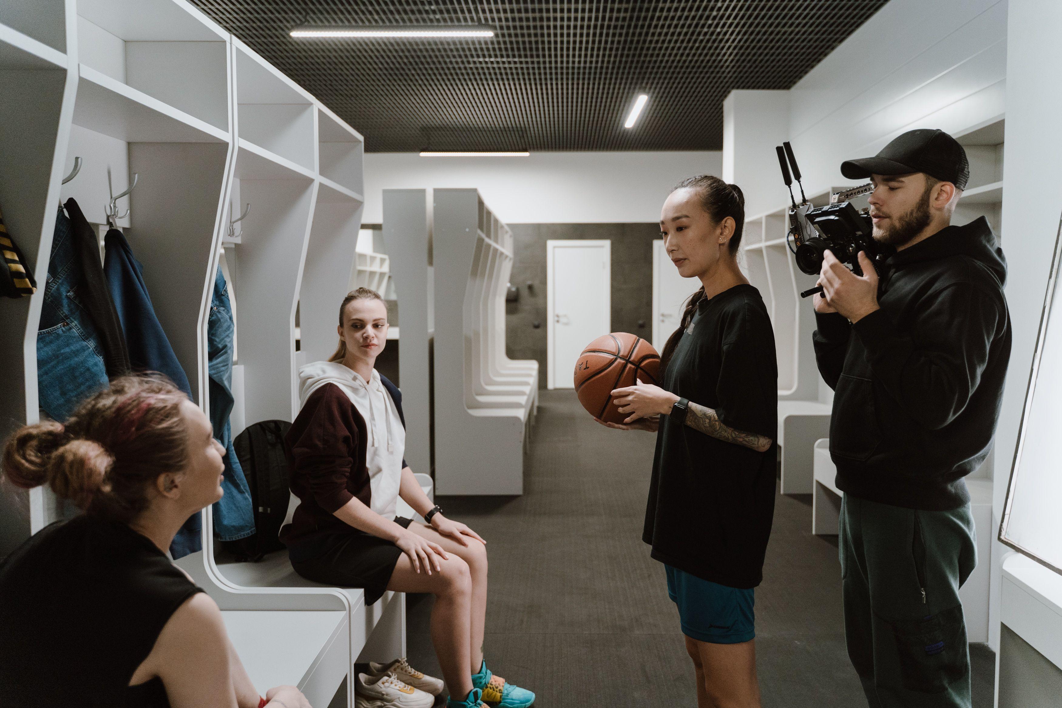 A candid behind-the-scenes look inside a basketball locker room during an interview with athletes and a cameraman.
