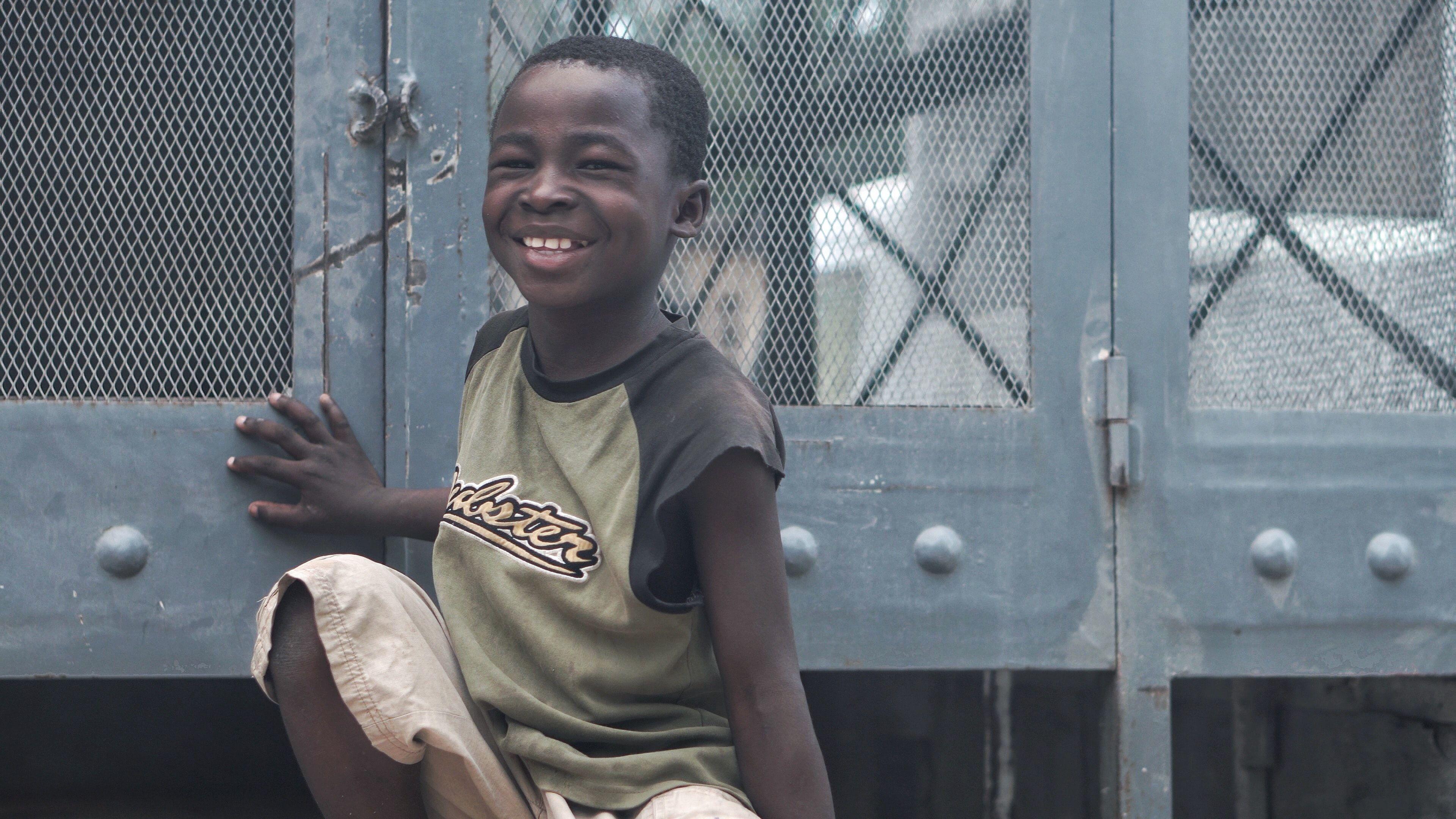 Happy child in Haiti smiles brightly while sitting outdoors.