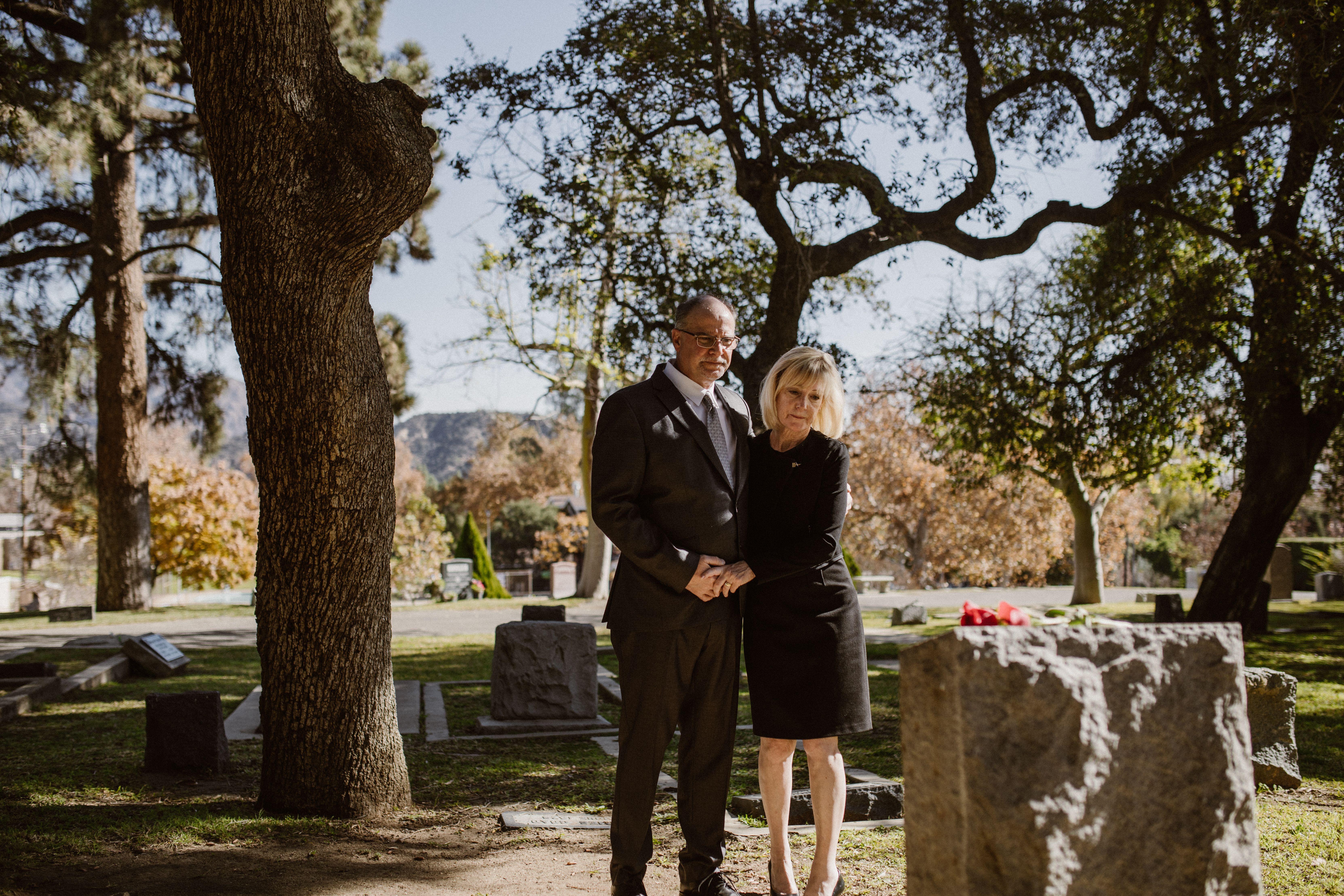 A couple stands solemnly in a serene cemetery, reflecting on memories and loss.