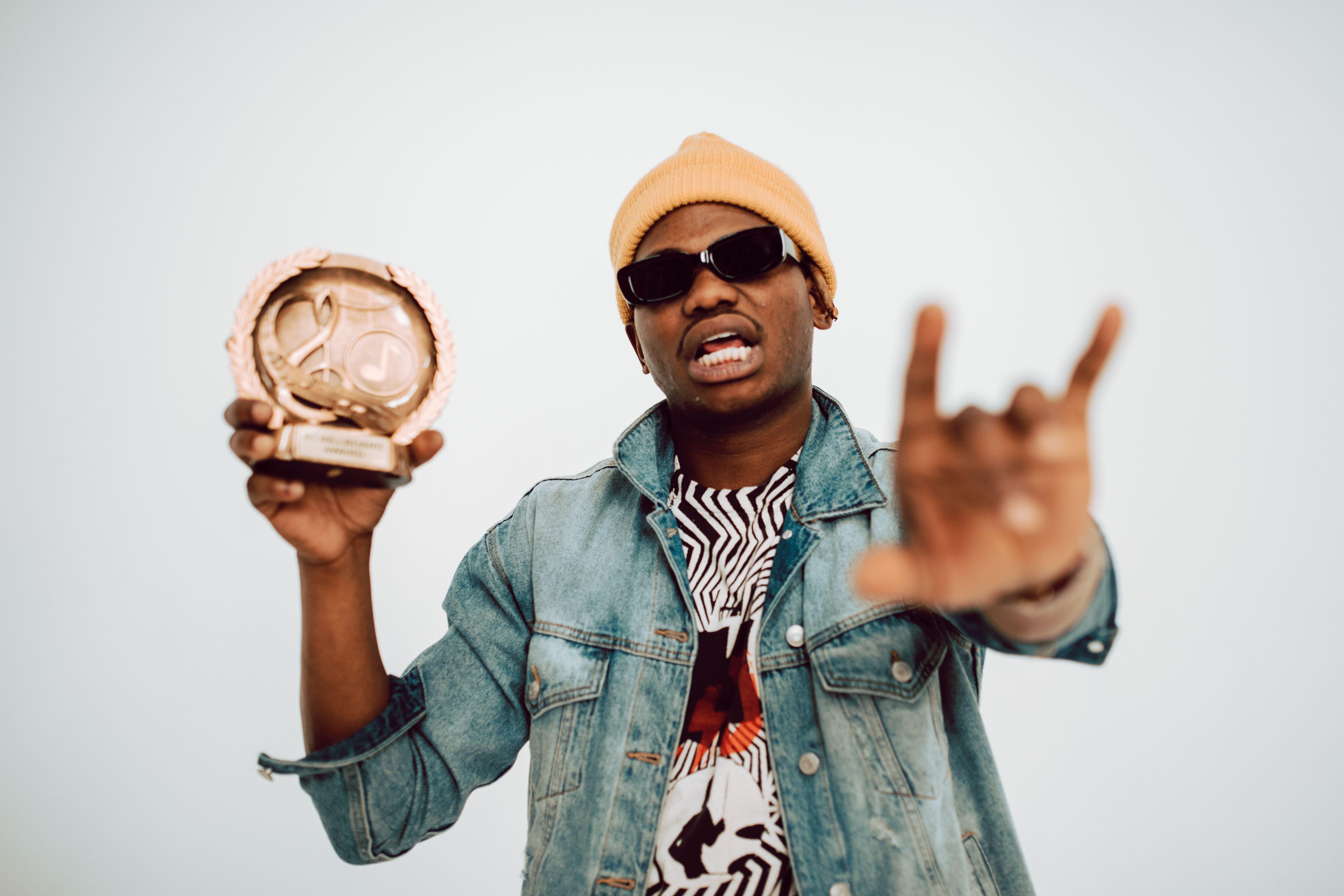 A man in casual attire celebrates his music award victory with a trophy in a studio setting.