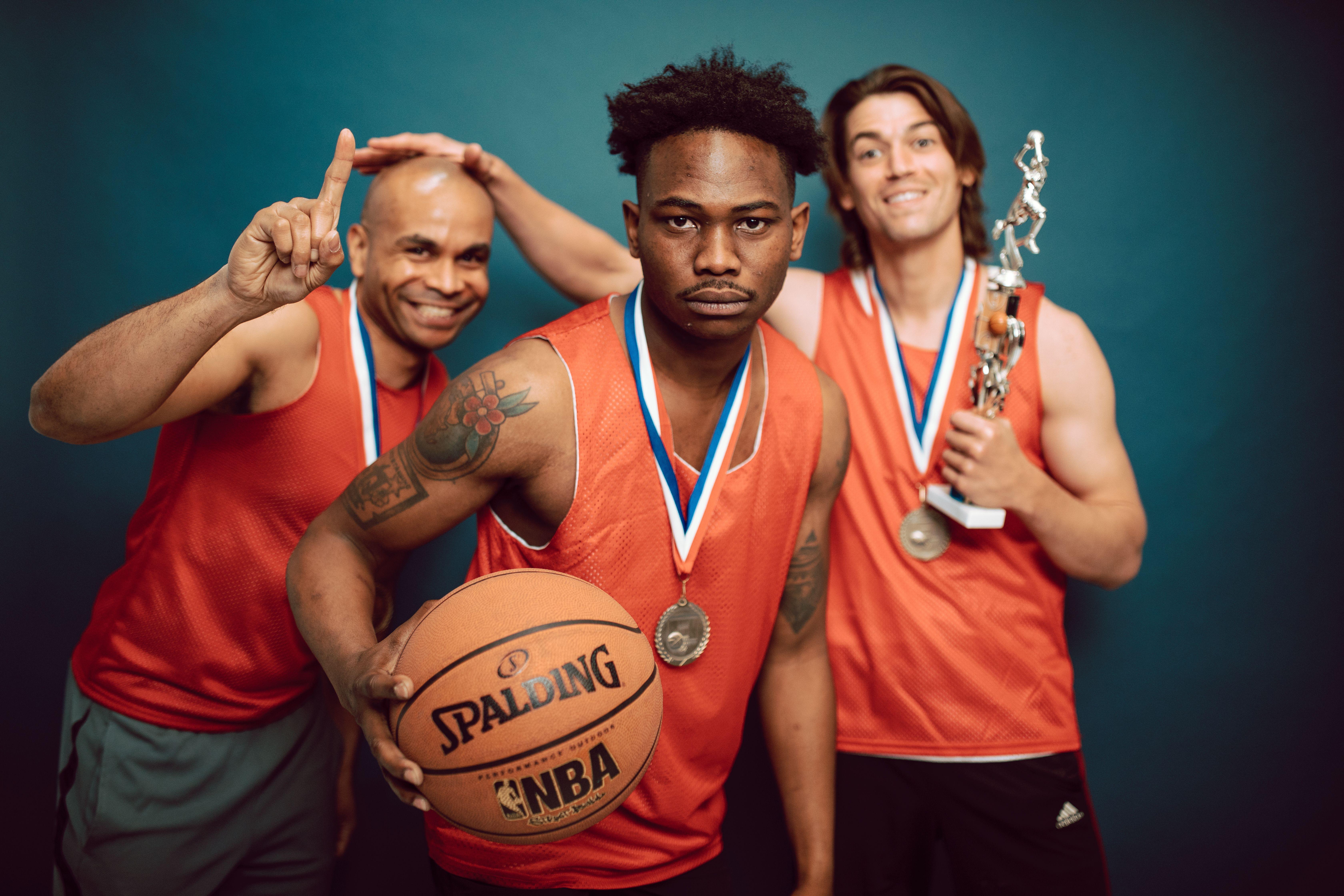 Three basketball players celebrating victory with trophies and medals, showcasing teamwork and accomplishment.