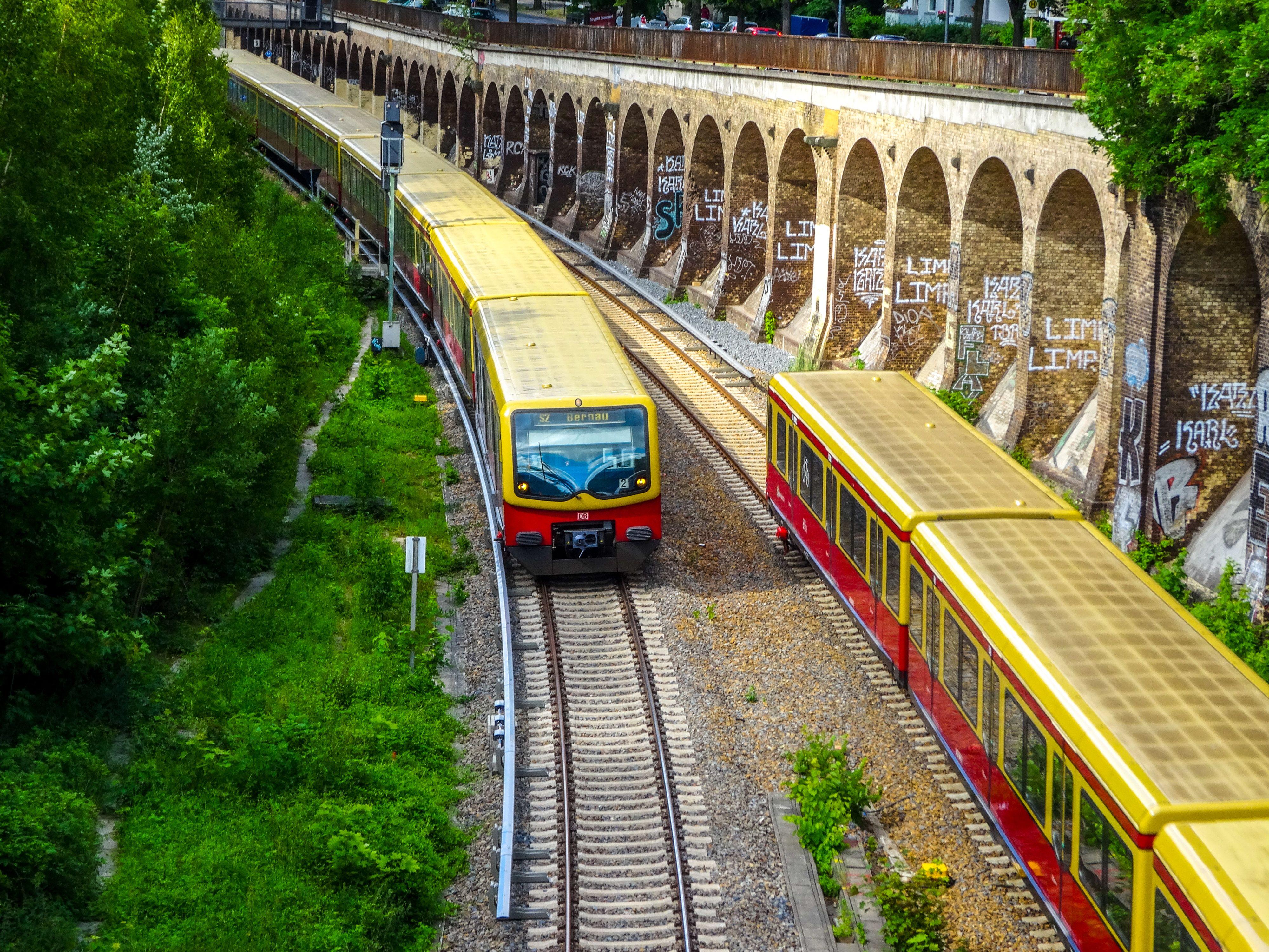 Colorful Berlin S-Bahn trains traveling on tracks beside graffiti-covered walls, capturing urban transit.