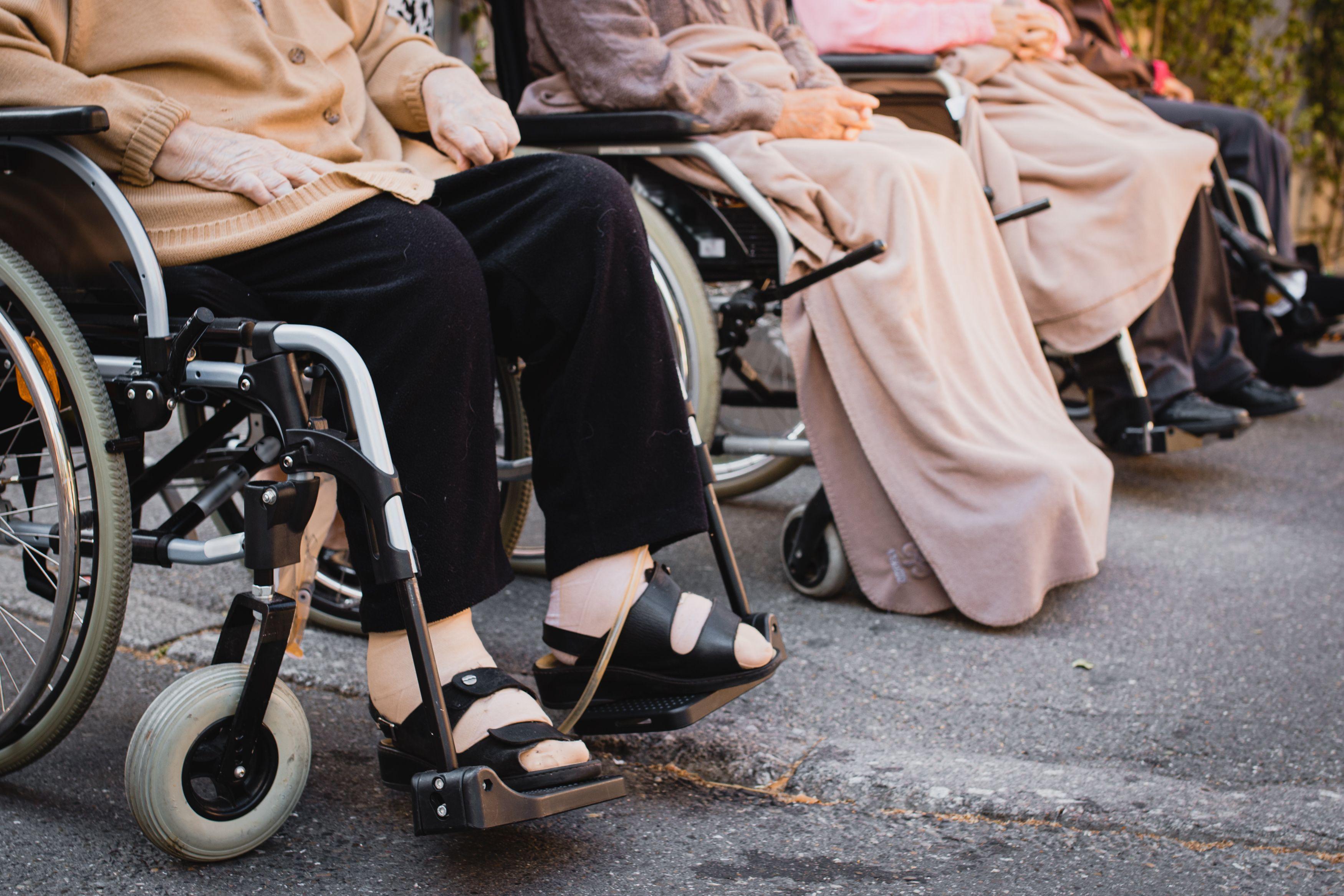 Senior adults sitting in wheelchairs outdoors enjoying a sunny day.