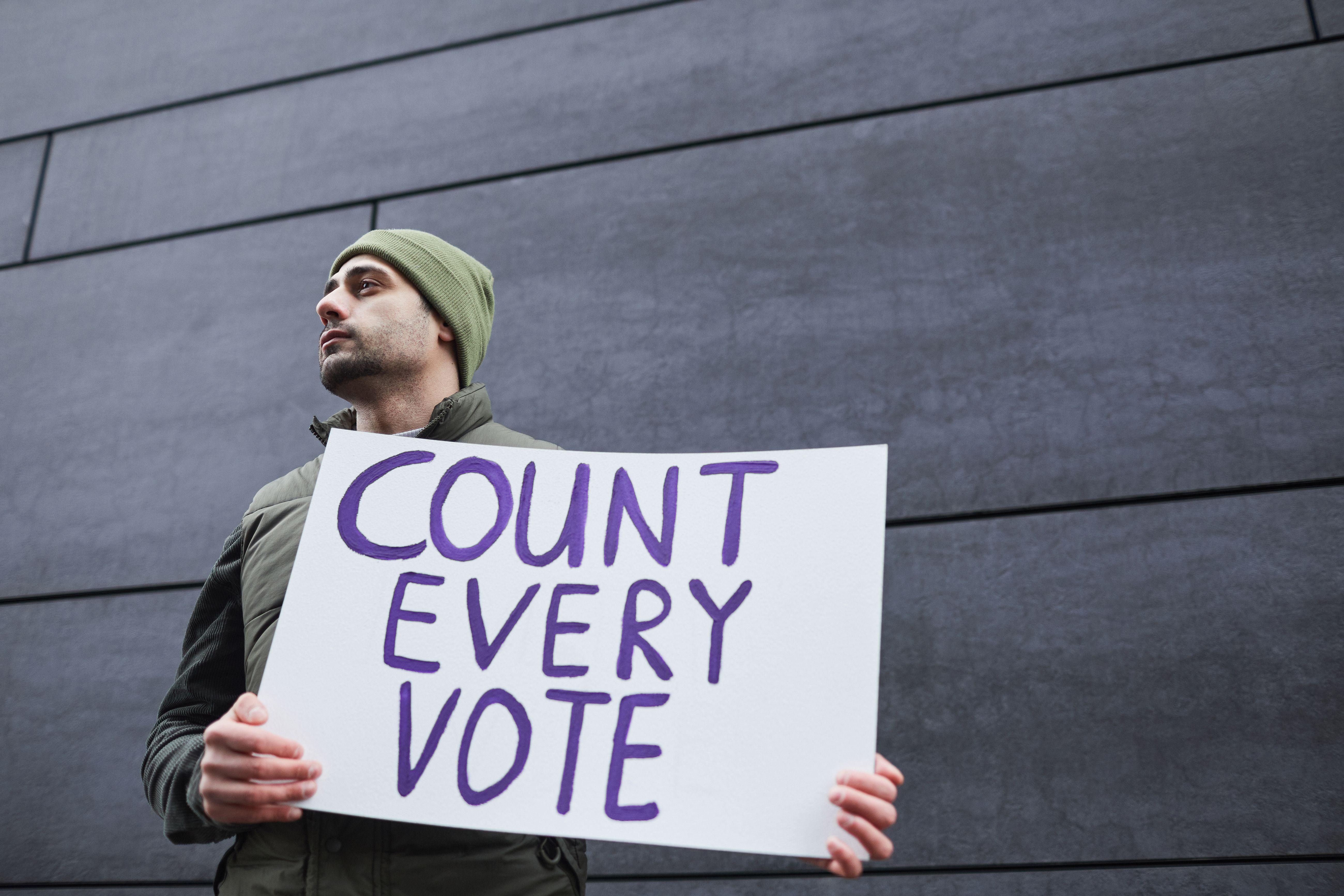 A man holding a 'Count Every Vote' placard, promoting democracy and voting rights.
