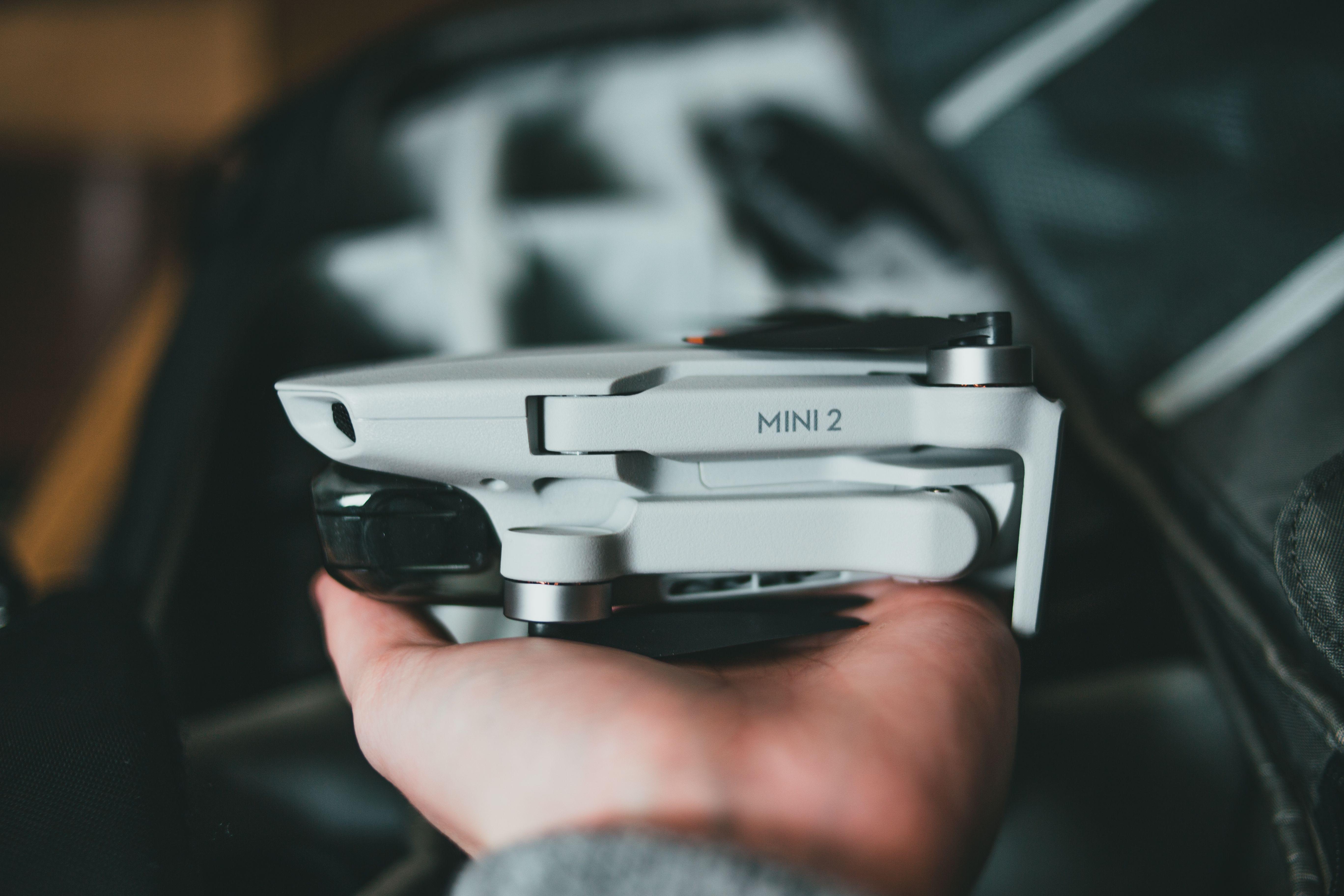 Crop anonymous male photographer holding modern compact white quadrocopter above bag with compartments on blurred background