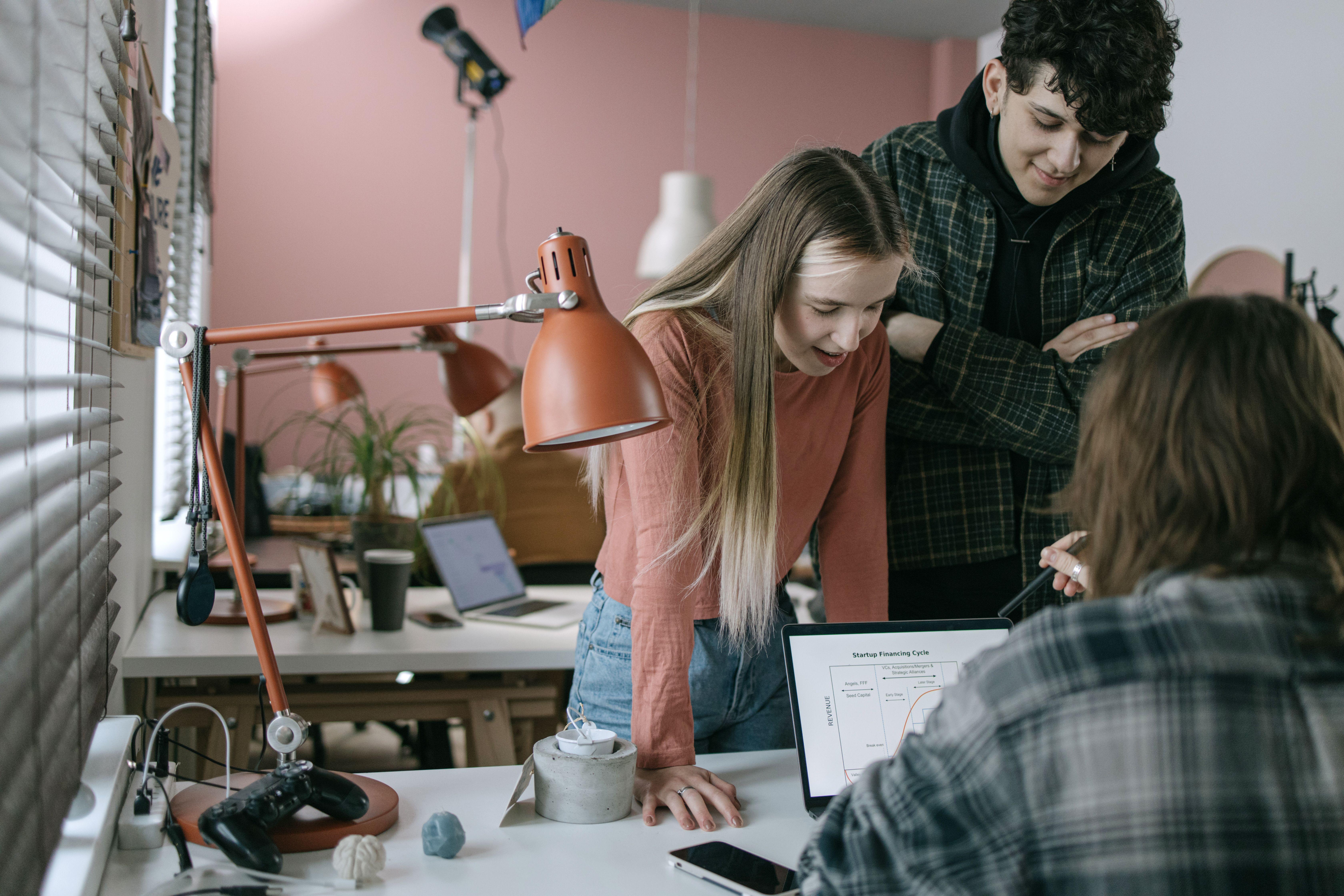 A group of young adults engage in a team meeting in a modern office, discussing ideas around a laptop.
