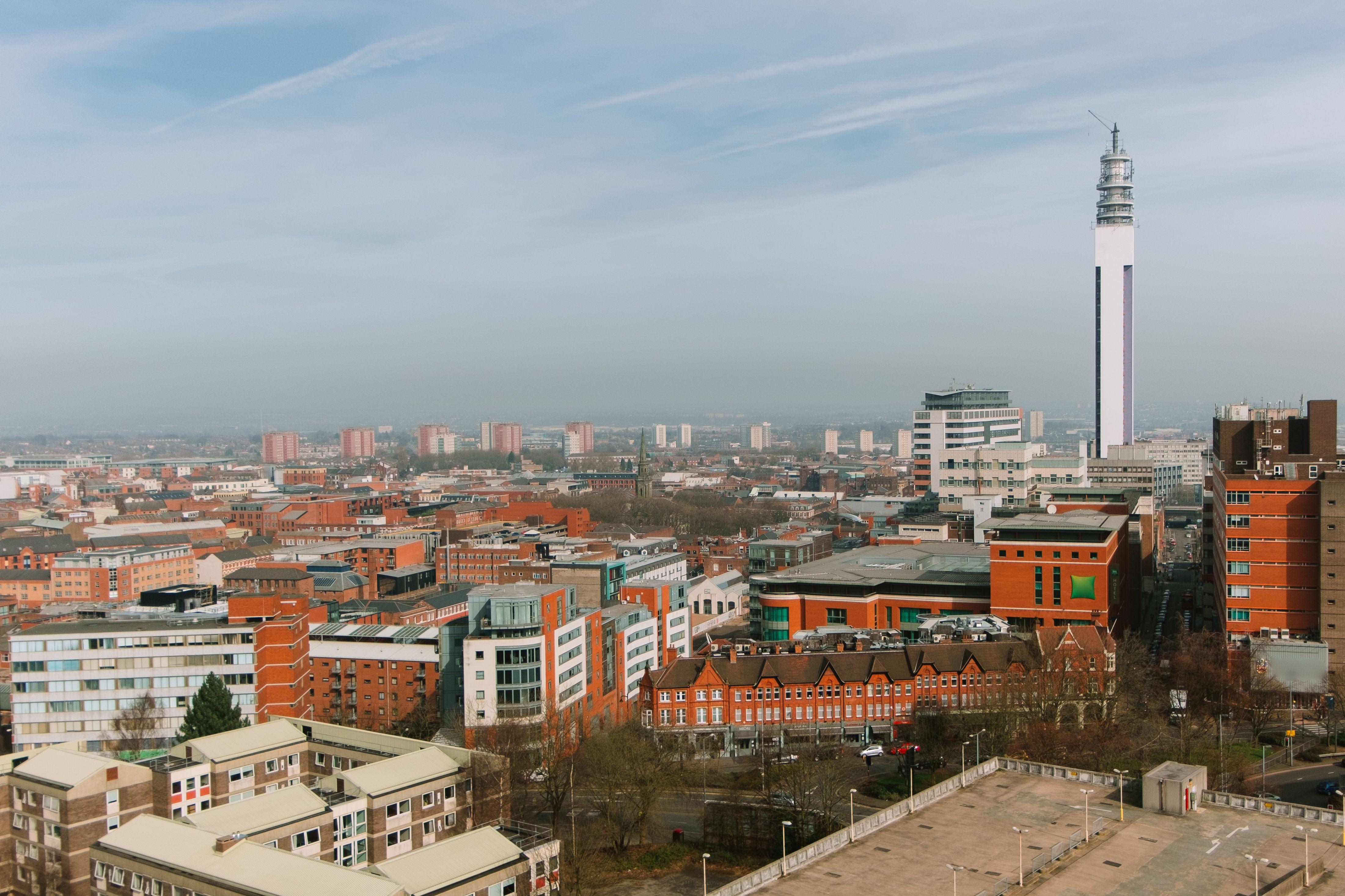 Tall industrial tower located amidst abundance of colorful residential houses with windows located on streets of city against blue sky