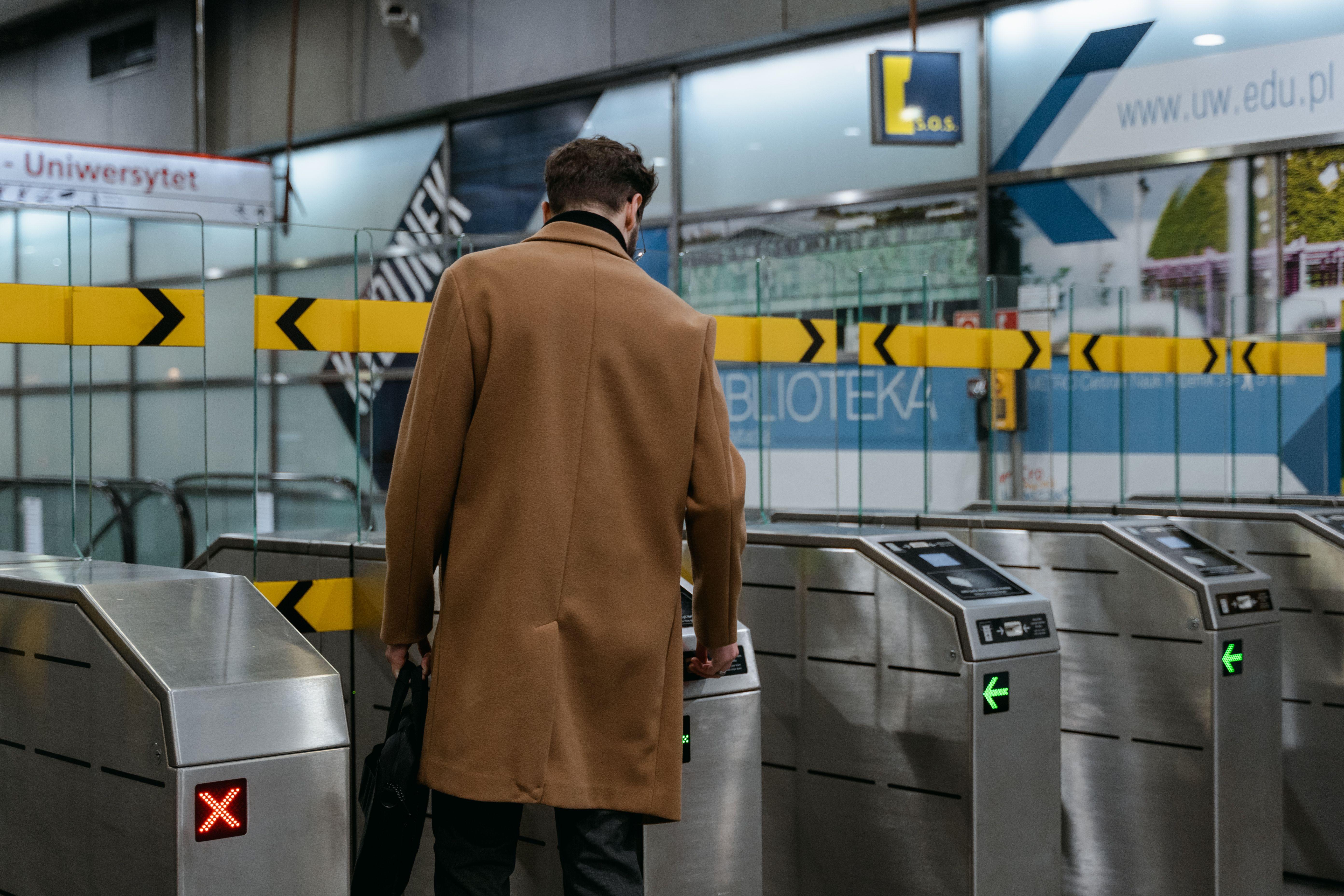 A commuter in a brown coat enters a metro station through ticket barriers.